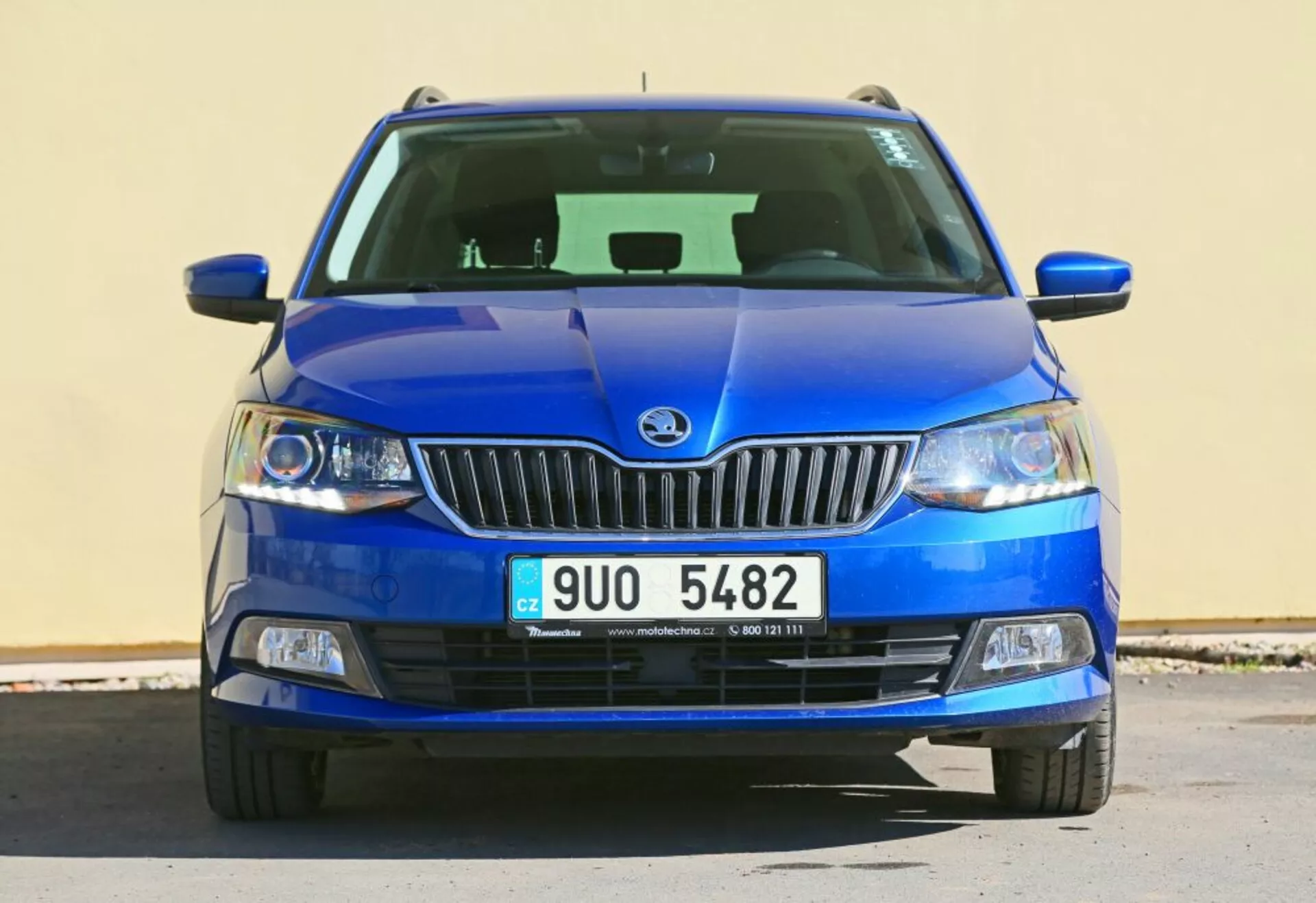 Vista frontal de um veículo azul Škoda apresentando o emblema da marca na grade cromada, faróis com lentes claras e luzes de nevoeiro em caixa preta, com uma grade inferior detalhada e design de capô esculpido.