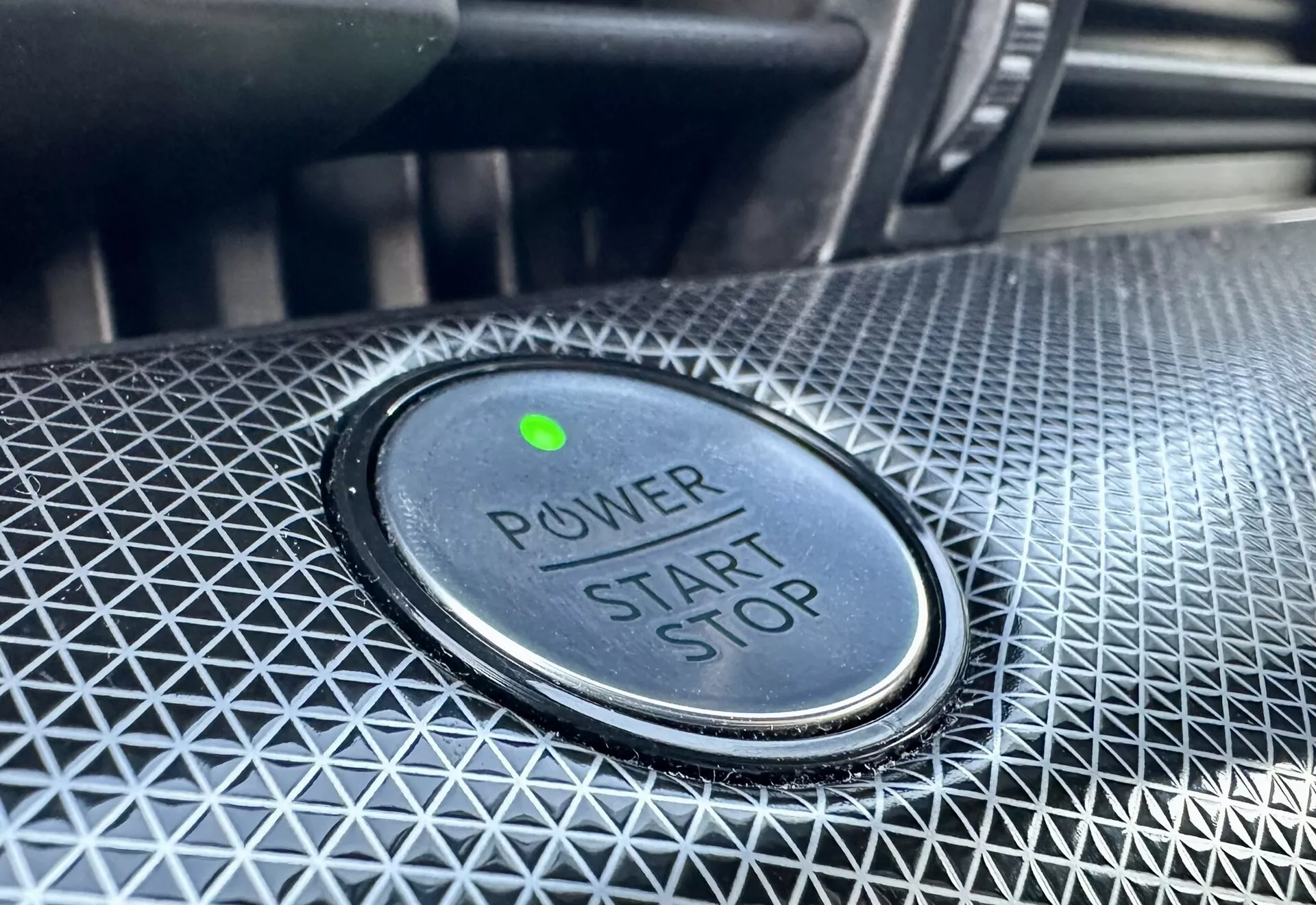 Vista aproximada do botão de ligar/desligar em um Ford Mustang-Mach-E 2020, apresentando o texto 'POWER START STOP', luz indicadora verde e design texturizado ao redor