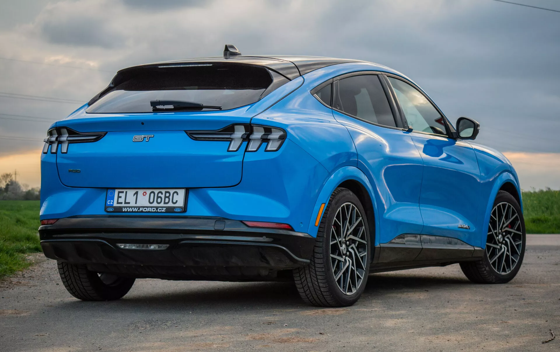 SUV elétrico azul Ford Mustang Mach-E 2020 mostrado de uma perspectiva traseira de três quartos, destacando seu design aerodinâmico elegante, luzes traseiras LED modernas, rodas de liga leve multiraiadas, emblema de veículo elétrico e características tecnológicas