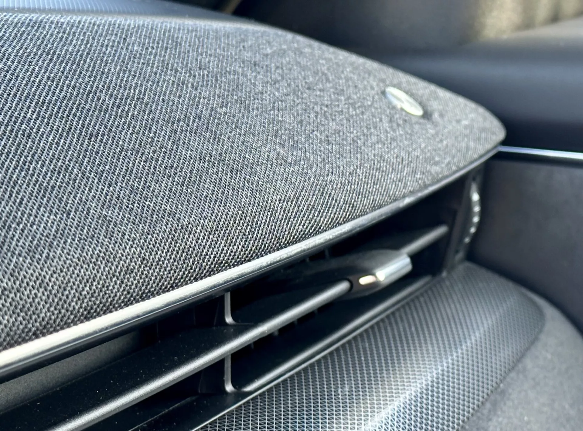 Vista de perto no interior do Ford Mustang Mach-E 2020 mostrando uma parte do painel de instrumentos ou painel da porta com uma grade de alto-falante de tecido premium integrada, um emblema sugerindo uma parceria com um fabricante de equipamento de áudio de alta qualidade, ao lado de uma ventilação de ar preta brilhante