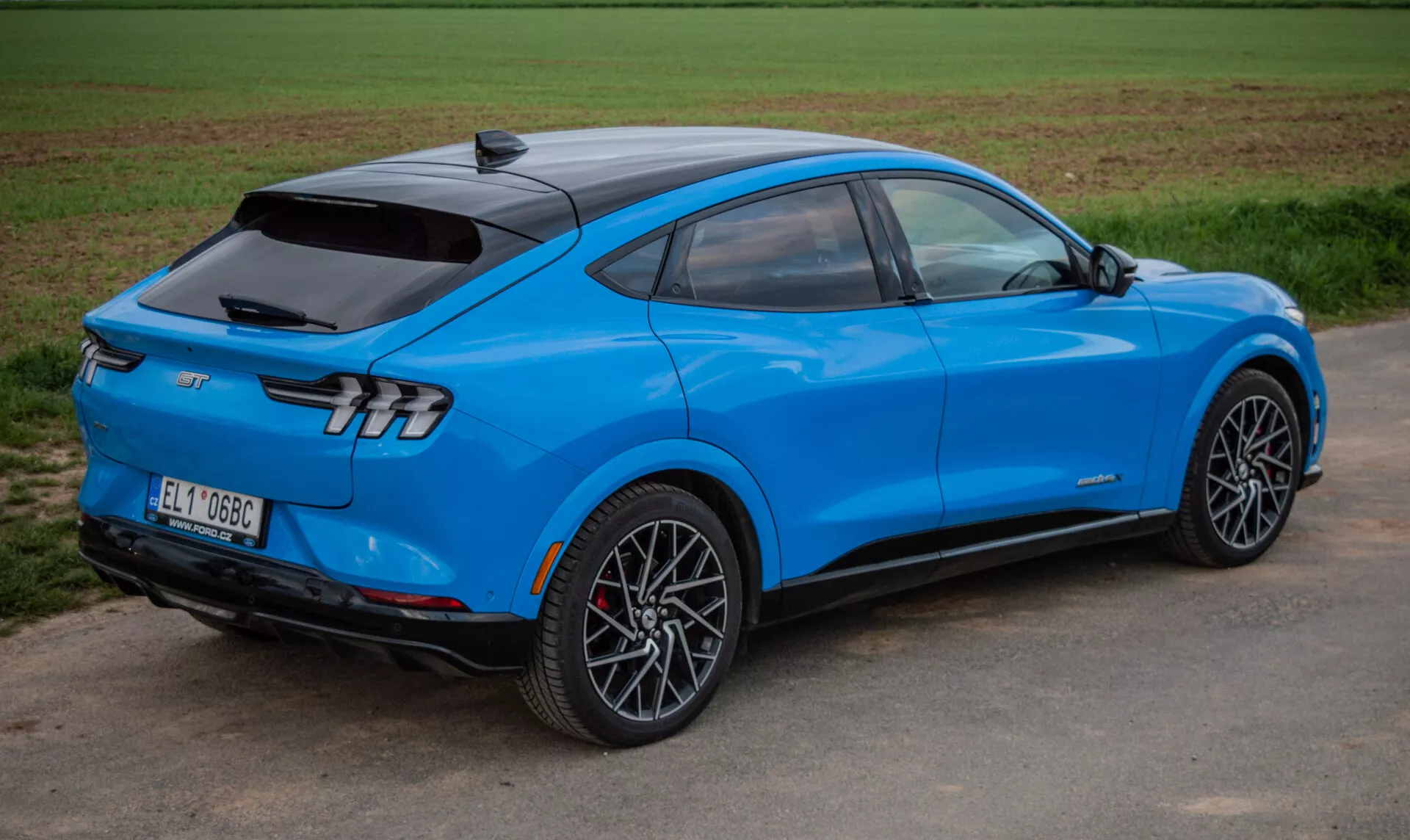 SUV elétrico Ford Mustang Mach-E 2020 azul brilhante em uma visão traseira dinâmica de três quartos destacando design aerodinâmico, luzes traseiras elegantes e rodas de liga leve esportivas, mostrando tecnologia avançada e propulsão elétrica.