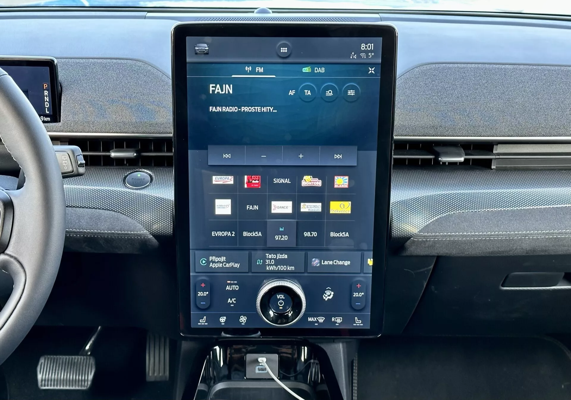 Console central interior do Ford Mustang Mach-E 2020 com um grande display sensível ao toque exibindo a interface multimídia com aplicativos e configurações, aberturas de ar integradas acima e um dial rotativo adicional para controle do clima abaixo.
