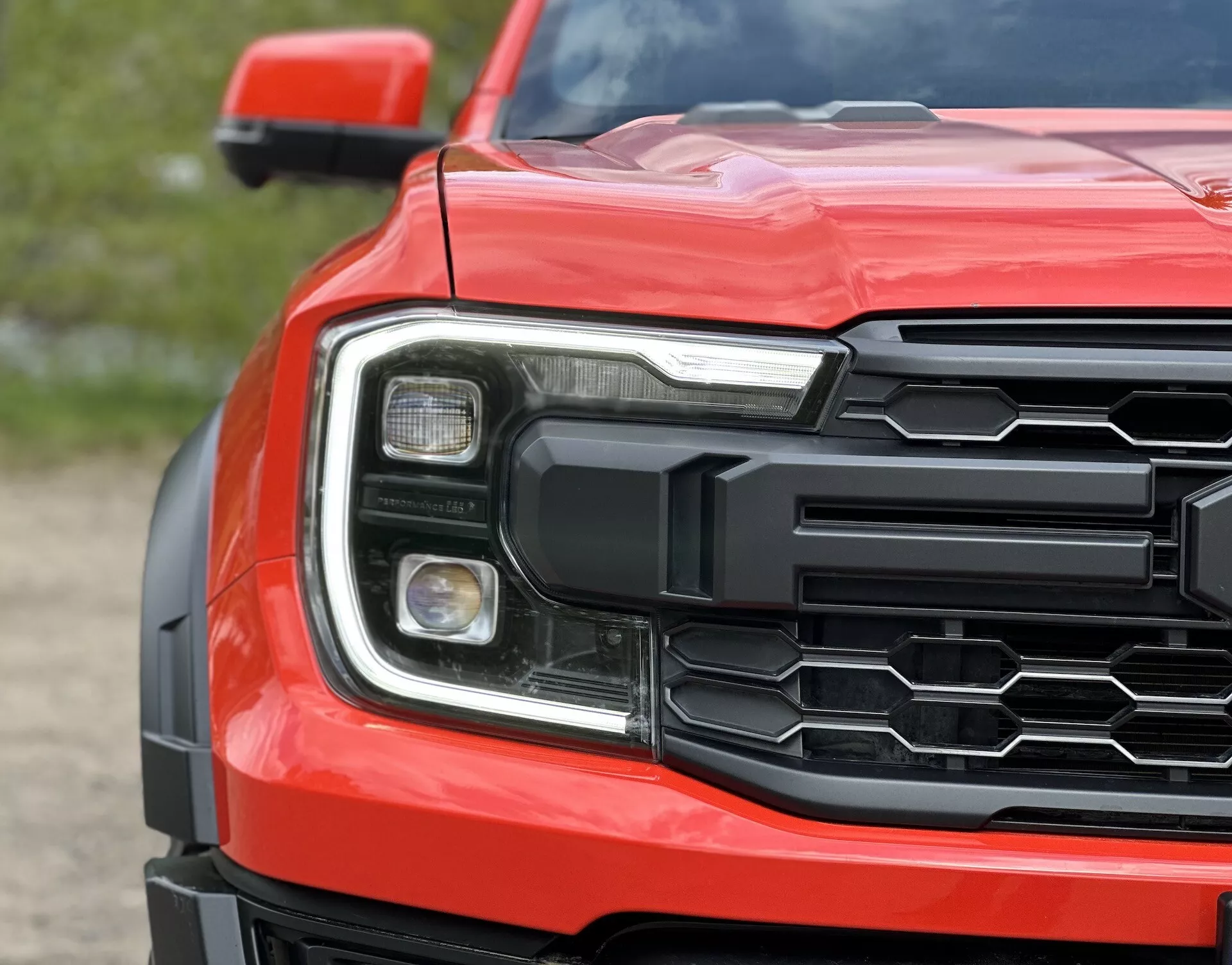 Vista de perto do canto frontal do Ford Ranger 2022 mostrando grade hexagonal, conjunto de farol detalhado e capô contornado em vermelho