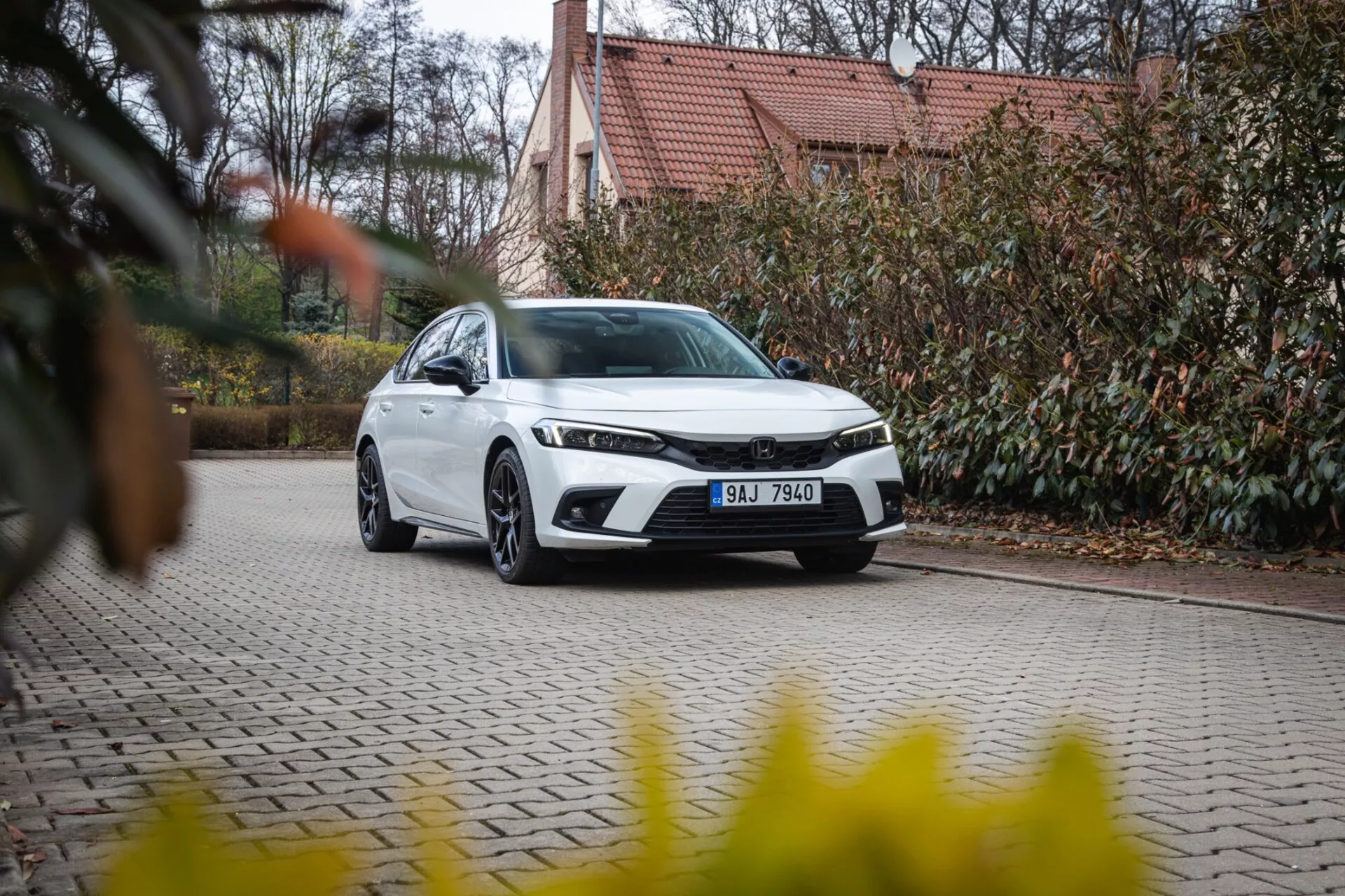Sedã moderno Honda Civic 2022 estacionado em entrada de calçada com paisagismo e edifício ao fundo, exibindo grade frontal, faróis de LED e design aerodinâmico elegante