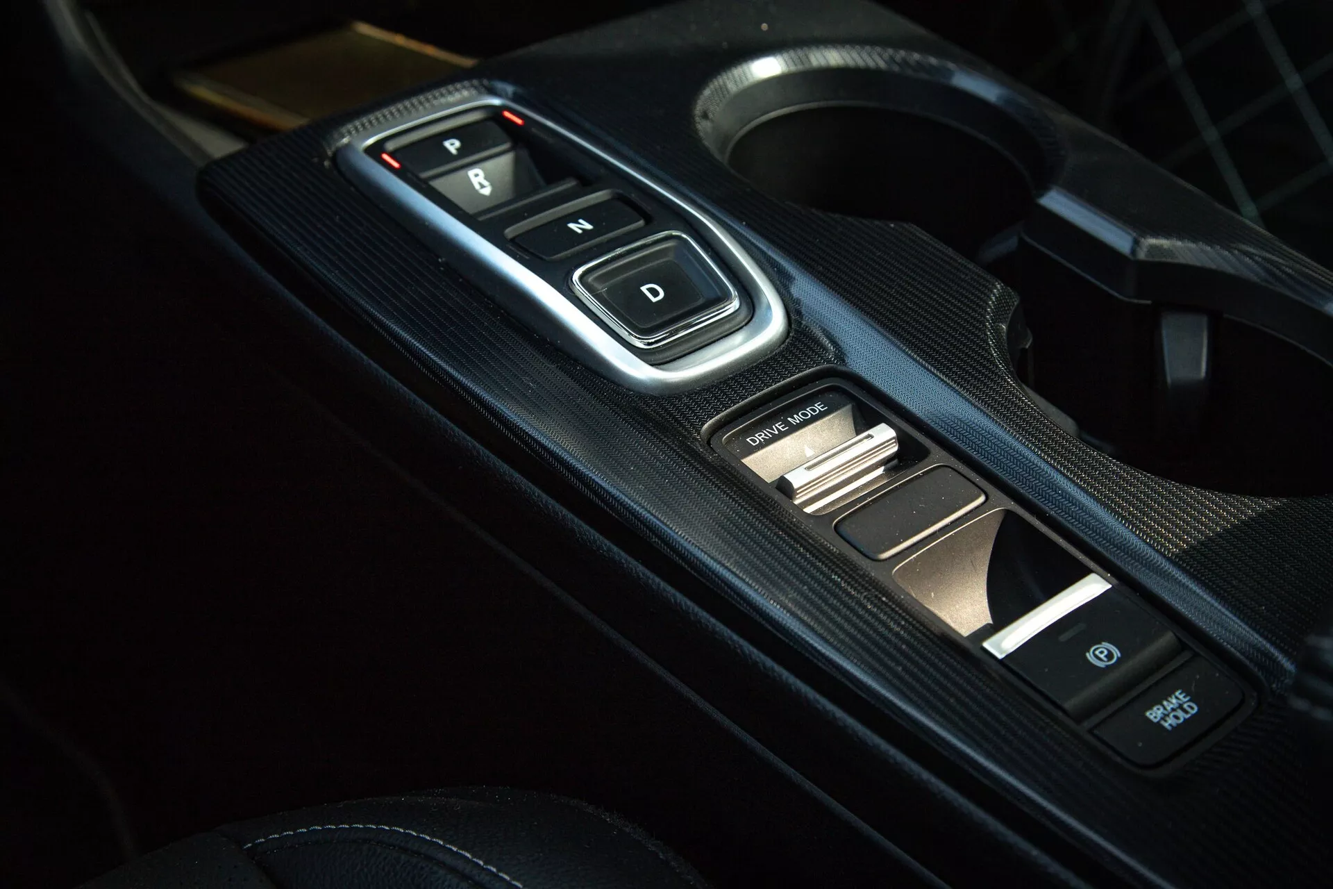 Close-up do interior do Honda Civic 2022 do console central com o seletor de marchas eletrônico com botões 'P, R, N, D', painel com textura de fibra de carbono e controles auxiliares, exibindo transmissão automática moderna e estética esportiva