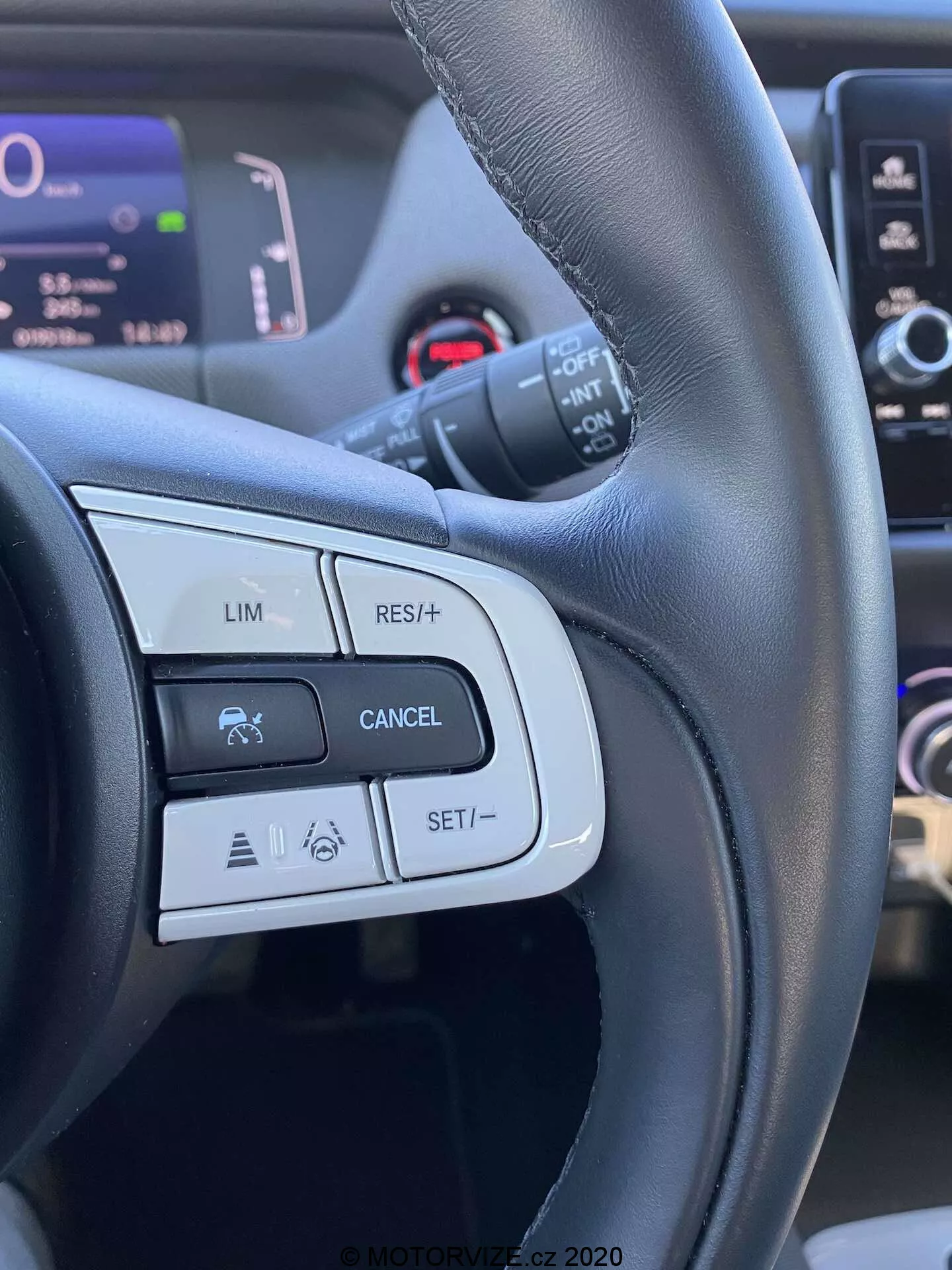 Vista detalhada dos controles do volante do Honda Jazz 2020 Crosstar, focando nos botões e recursos do lado esquerdo, como LIM (limitador de velocidade), RES/+ (retomar ou aumentar a velocidade), CANCEL e SET/- (definir ou diminuir a velocidade). A imagem é tirada da perspectiva do motorista, destacando um volante de couro preto com acabamentos foscos e brilhantes, e mostrando ícones relacionados ao controle de cruzeiro e possivelmente a sistemas avançados de assistência ao motorista.