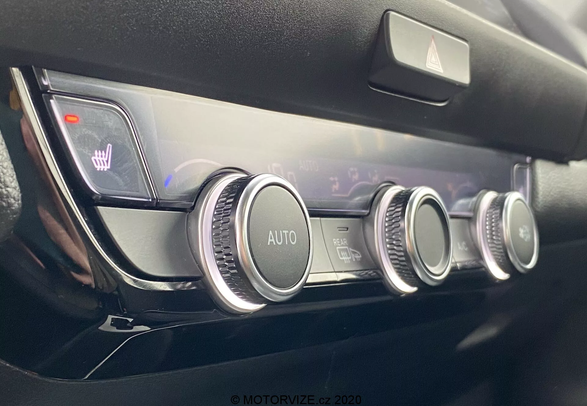 Vista aproximada do painel de controle climático moderno do Honda Jazz 2020, apresentando três botões circulares com acabamento metálico, um sistema de controle climático automático, configurações de temperatura de duas zonas indicadas em um display digital e ícones iluminados de aquecimento dos assentos, tudo em um design minimalista e de alta qualidade do painel.