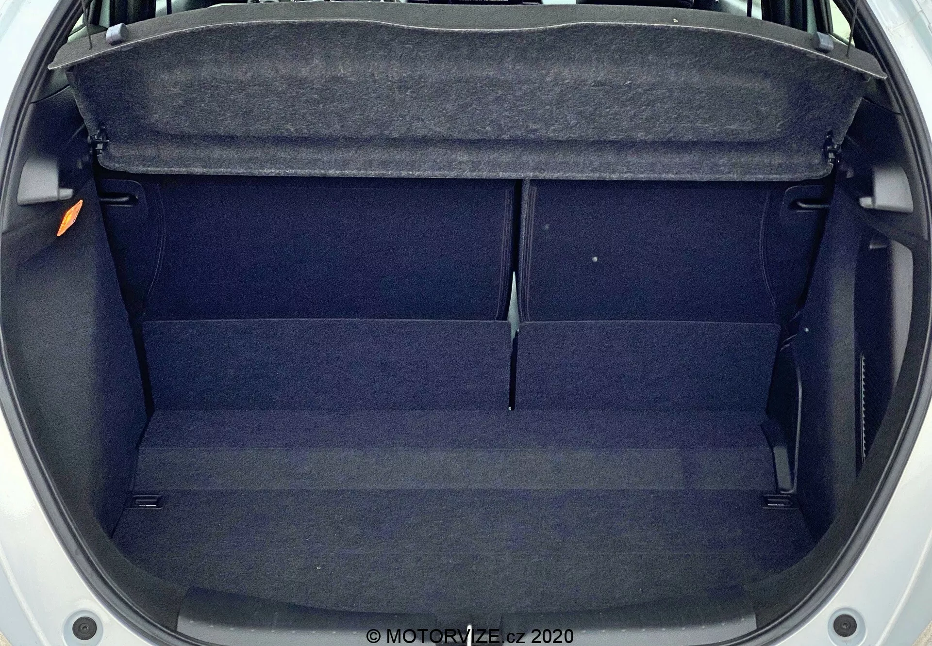 Vista aérea do porta-malas vazio do Honda Jazz 2020, mostrando um espaço retangular de tamanho moderado com forro de tecido escuro. As características incluem uma prateleira na parte superior, acabamentos internos nas laterais e uma ligeira elevação no centro. O porta-malas está limpo, desobstruído e parece bem conservado.