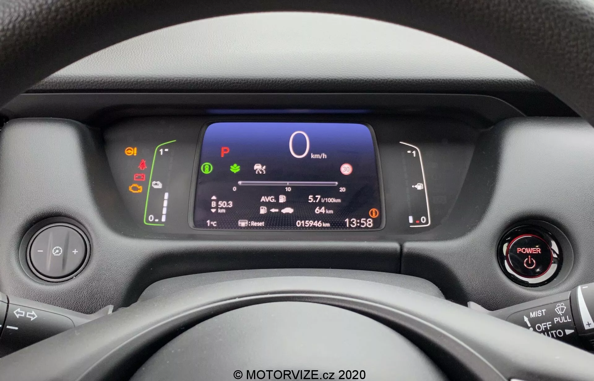 Vista do assento do motorista de um Honda Jazz 2020, focando no moderno painel de instrumentos, volante e controles do painel. O display digital mostra informações chave do veículo, incluindo velocidade, seleção de marcha, eficiência de combustível, hora e temperatura, com ignição sem chave e controles multifuncionais no volante visíveis.