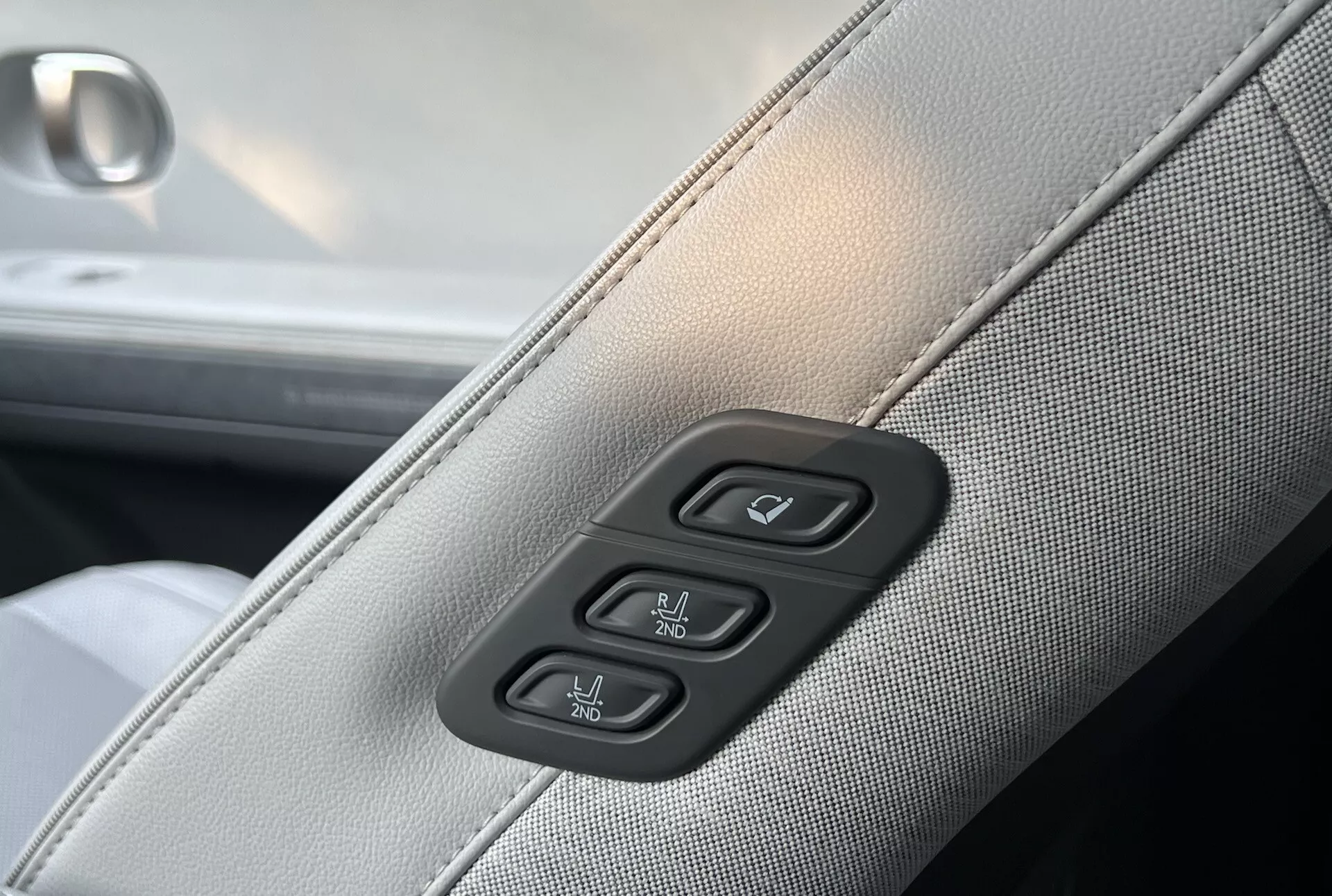 Detalhe do interior do Hyundai Ioniq-5 2021 mostrando estofamento sintético ou de couro em cinza claro com costuras em cinza escuro e controles para janelas e travas de porta elétricas em um fundo preto de piano