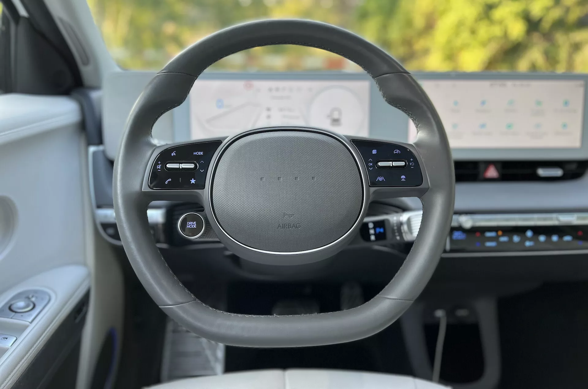 Visão interior do Hyundai Ioniq-5 2021 com foco no volante de design premium e painel digital de alta resolução pela perspectiva do motorista, exibindo controles sensíveis ao toque multifuncionais e recursos de tecnologia avançada