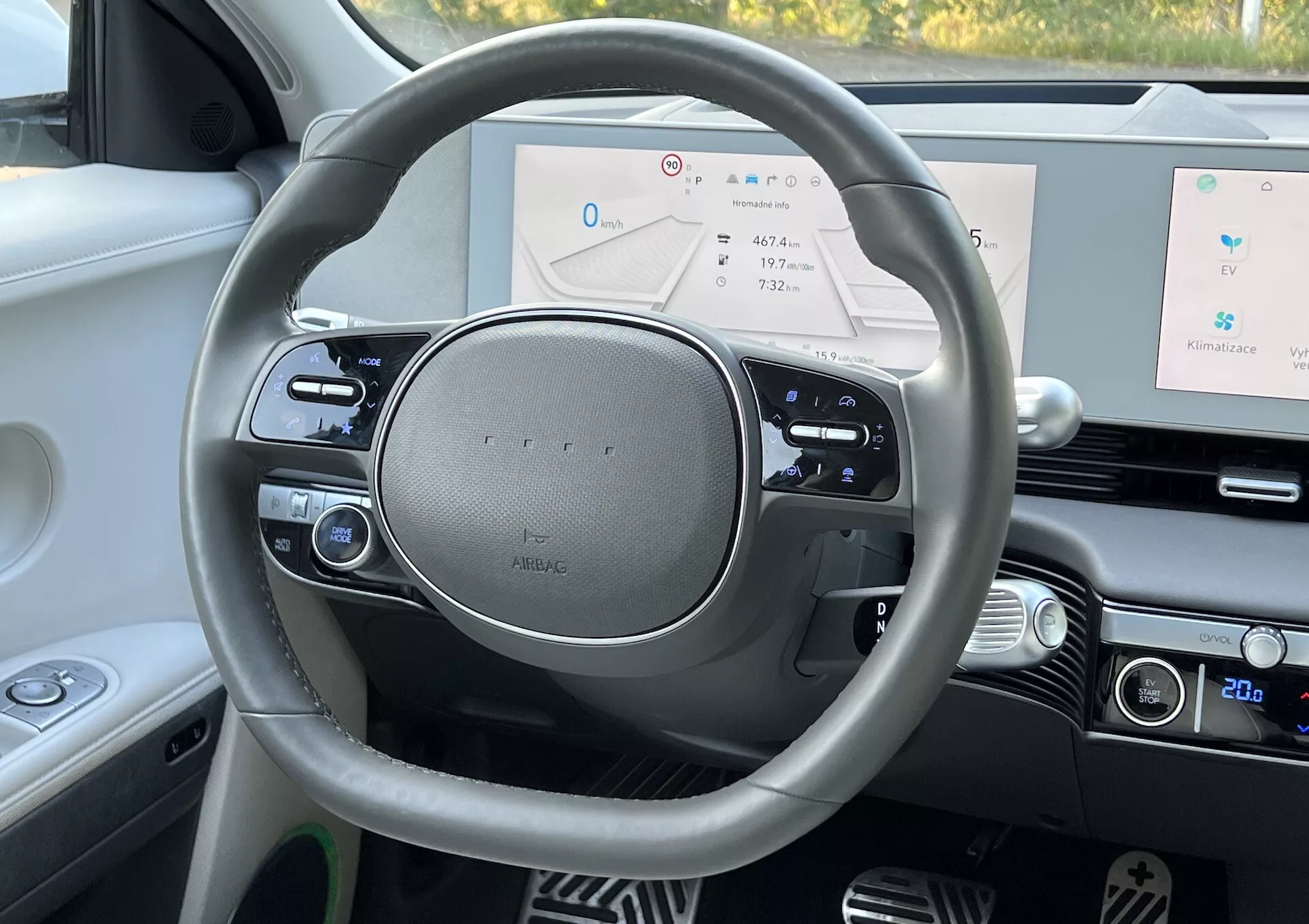Perspectiva em primeira pessoa do interior do Hyundai Ioniq 5 2021 focando no volante moderno com emblema de prata, painel digital exibindo velocímetro, navegação e status do sistema, ao lado de detalhes de design interior de alta qualidade