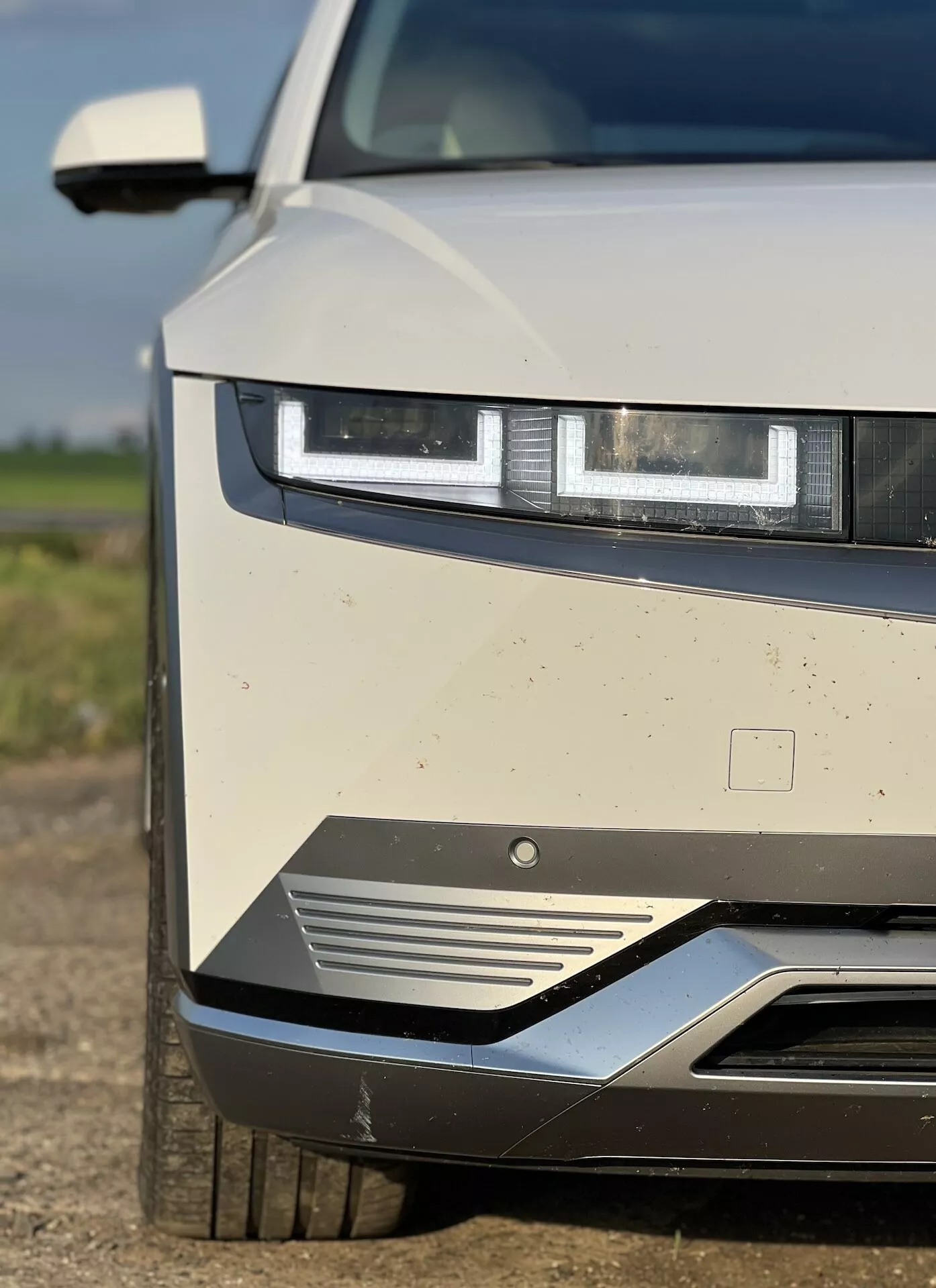 Visão detalhada do Hyundai Ioniq 5 2021 destacando os faróis LED, design da grade frontal e características aerodinâmicas, com sujeira visível indicando uso recente