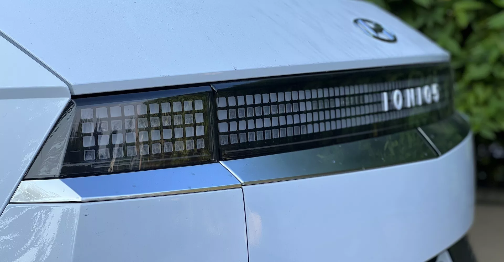 Imagem aproximada do conjunto de luzes traseiras e detalhe do porta-malas de um Hyundai Ioniq-5 2021 a partir de um ângulo baixo, destacando a assinatura de luz LED linear e design moderno.