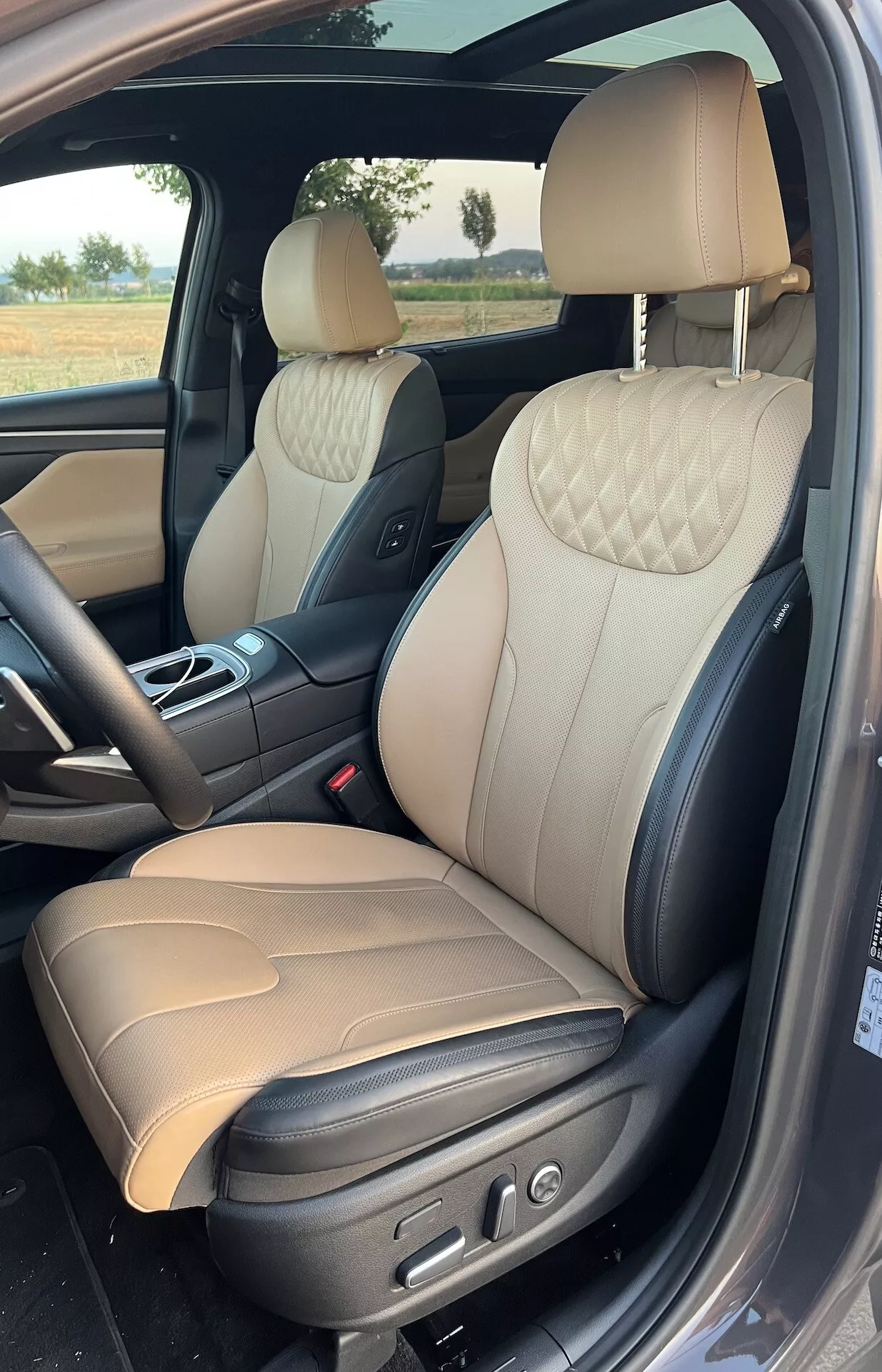 Vista interior de um Hyundai Santa Fe 2020, destacando a área luxuosa do passageiro dianteiro com assentos em couro de dois tons com costura acolchoada em diamante, controles ajustáveis eletronicamente e materiais sofisticados como acabamentos em metal escovado e maçanetas cromadas.