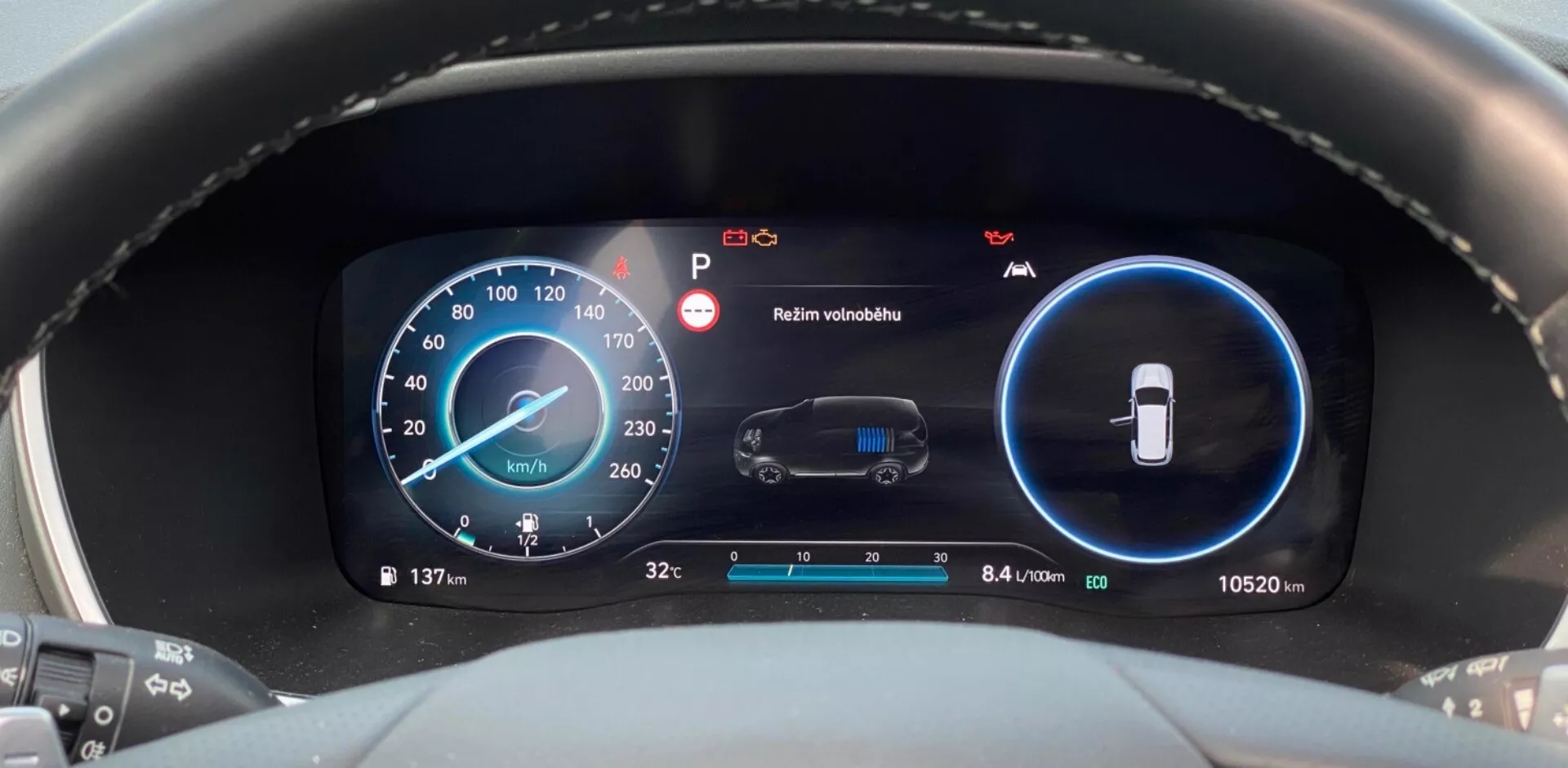 Vista de perto do painel de instrumentos digital moderno de um Hyundai Santa Fe 2020, tirada da perspectiva do motorista. Focando na área do painel, a imagem apresenta dois principais displays digitais em azul e preto. O display à esquerda é um velocímetro que mostra 137 km/h com indicadores adicionais de RPM. O display à direita monitora o status do veículo, incluindo um alerta de manutenção e um aviso de 'Manter visibilidade'. A seção inferior mostra a temperatura externa (3,2°C) e o hodômetro (10.520 km), junto com uma métrica de eficiência de 8,4 litros por 100 quilômetros.