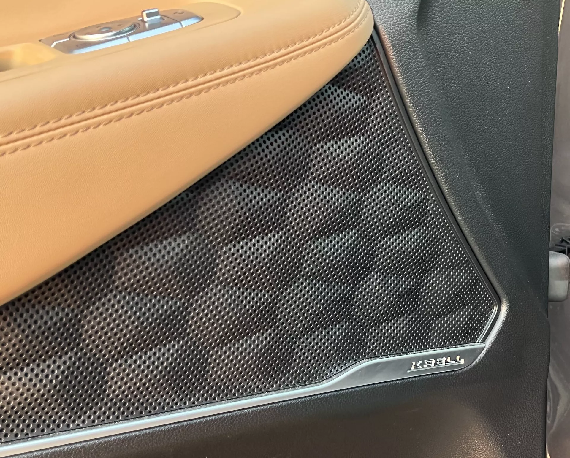 Vista de close-up do painel da porta interna do Hyundai Santa Fe 2020, focando na transição entre a estofaria de couro bege com costura contrastante e a grade do alto-falante Bowers & Wilkins. A cobertura do alto-falante texturizada e perfurada com o emblema cromado Bowers & Wilkins destaca o sistema de áudio premium e os materiais de luxo do veículo.