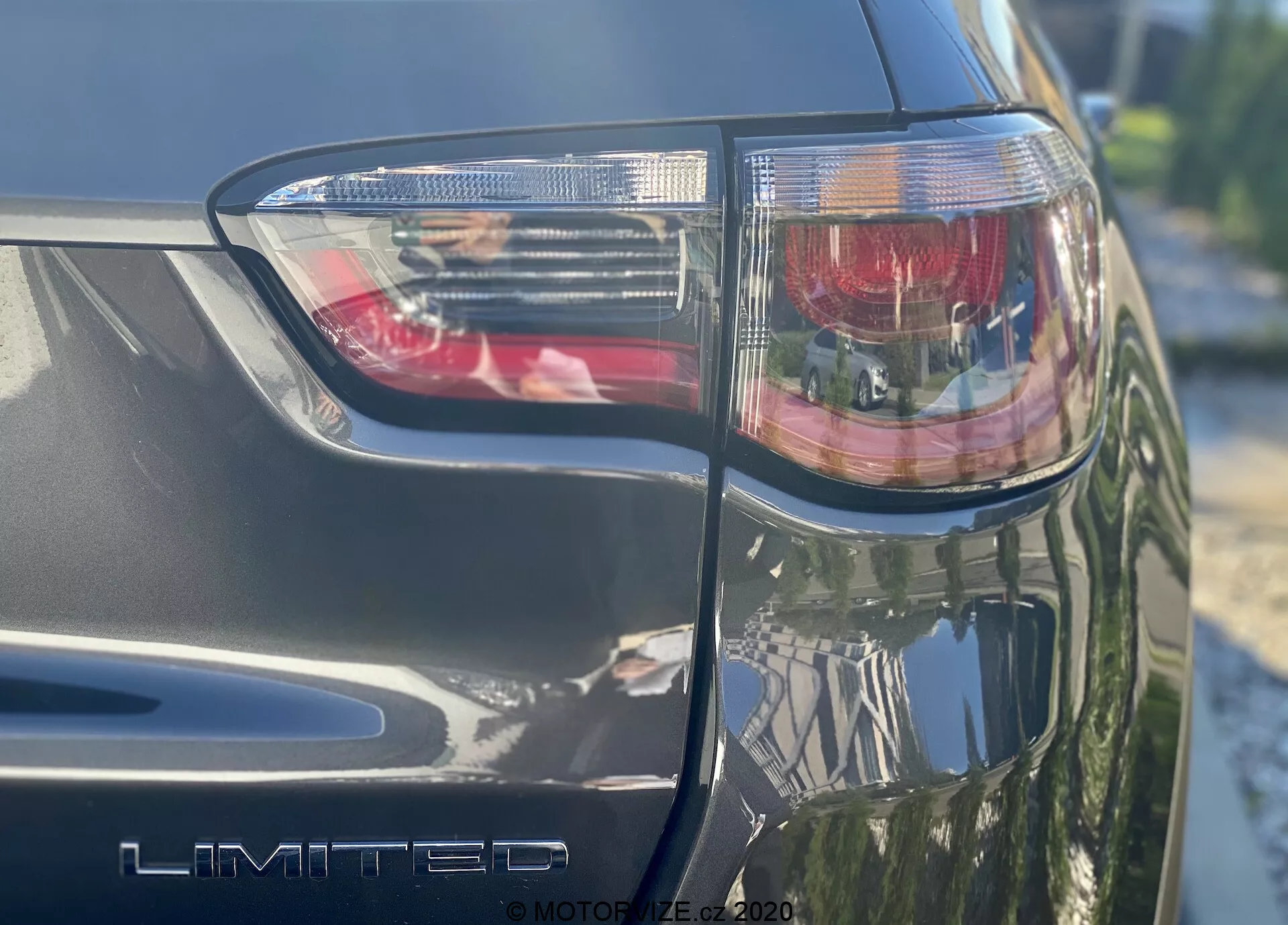 Uma foto em close e em ângulo da parte traseira esquerda de um Jeep Compass 2017, apresentando o conjunto de luzes traseiras com luz de freio vermelha e seções claras, exibindo proeminentemente o emblema 'LIMITED'. O acabamento metálico e os ângulos nítidos do design com tecnologia de iluminação LED são visíveis, tirada em um dia ensolarado.