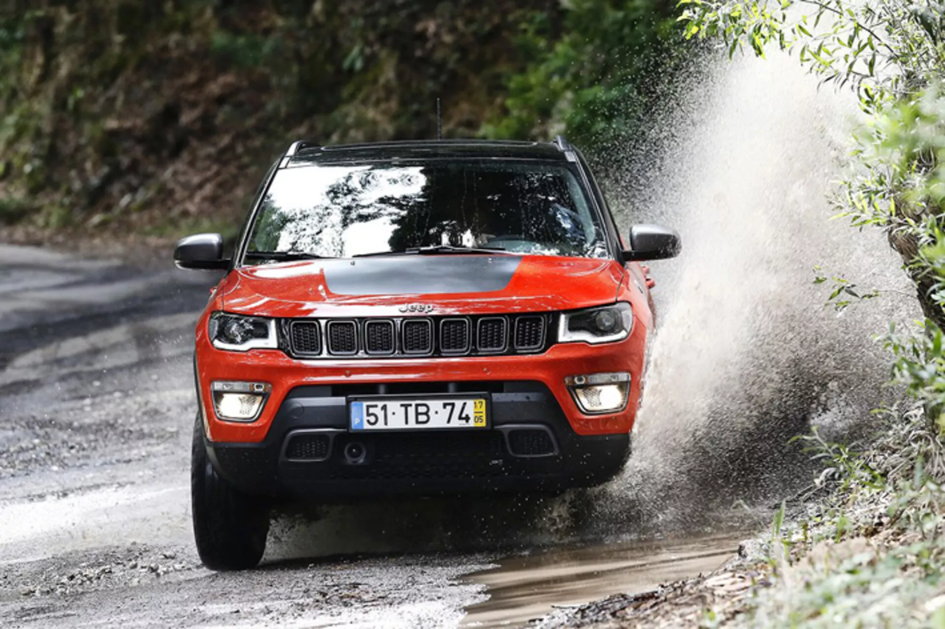 SUV Jeep Compass 2017 em ação dinâmica off-road, exibido de um ângulo frontal de três quartos enfatizando seu design robusto e capacidades de desempenho numa trilha florestal lamacenta.