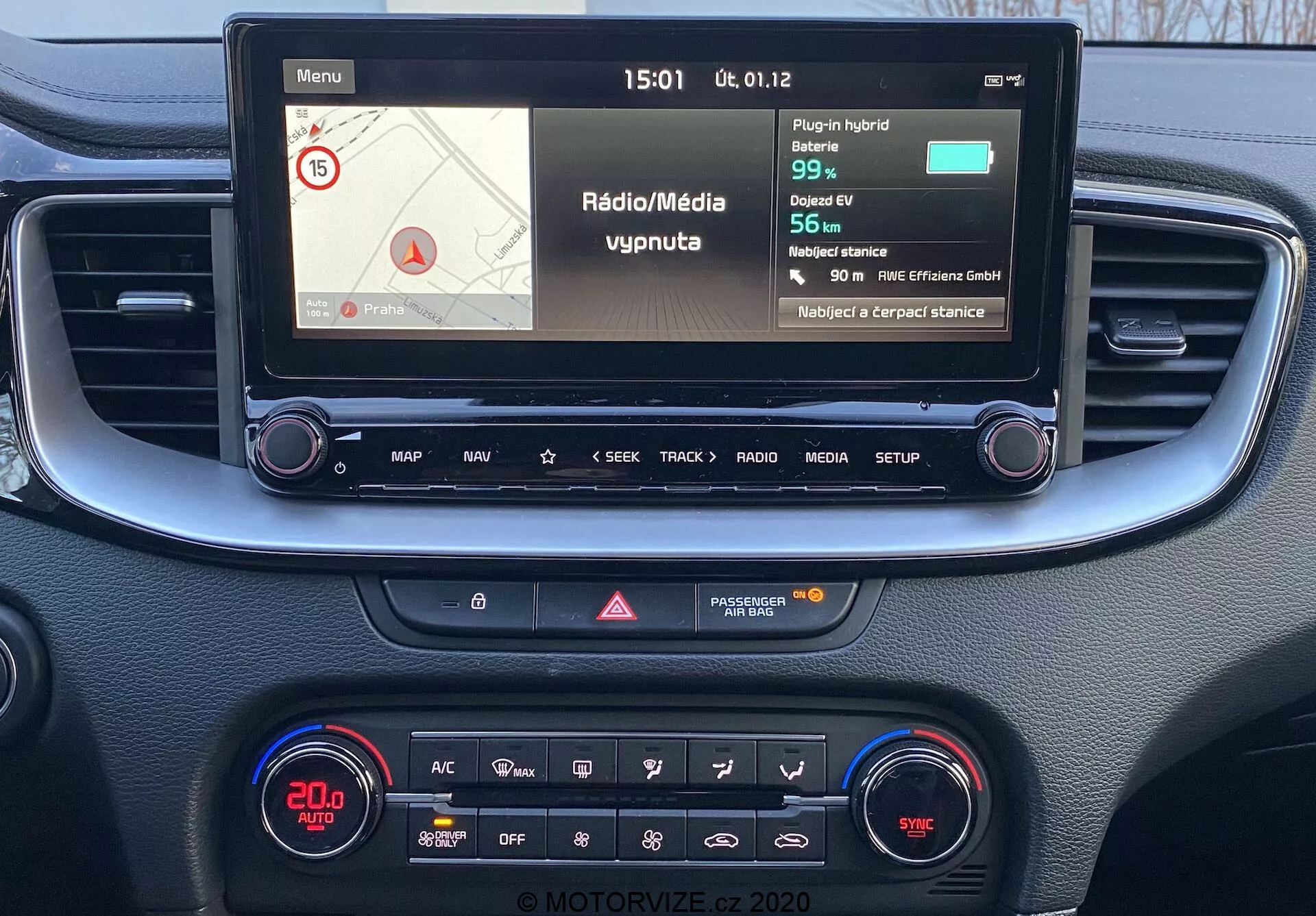 Perspectiva em primeira pessoa da consola central e do sistema de infoentretenimento do Kia Ceed 2018, com um ecrã a cores a mostrar informações de navegação e media, botões físicos para controlo e um painel de controlo do clima com ecrã digital e várias funcionalidades.