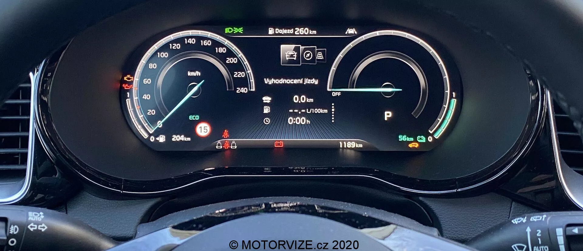 Vista aproximada do painel de instrumentos digital do Kia Ceed 2018 a partir do assento do motorista. A tela inclui um velocímetro com um ponteiro físico e uma leitura digital que mostra 15 km/h. À direita, há um medidor de energia/bateria indicando uma bateria cheia com um alcance de 481 km. Outros elementos incluem uma tela de status de pronto, informações do motorista com luzes de advertência, uma leitura de temperatura externa de 20,5°C e o veículo no modo Park. O arco superior do volante é visível, com um design esportivo de fundo plano.