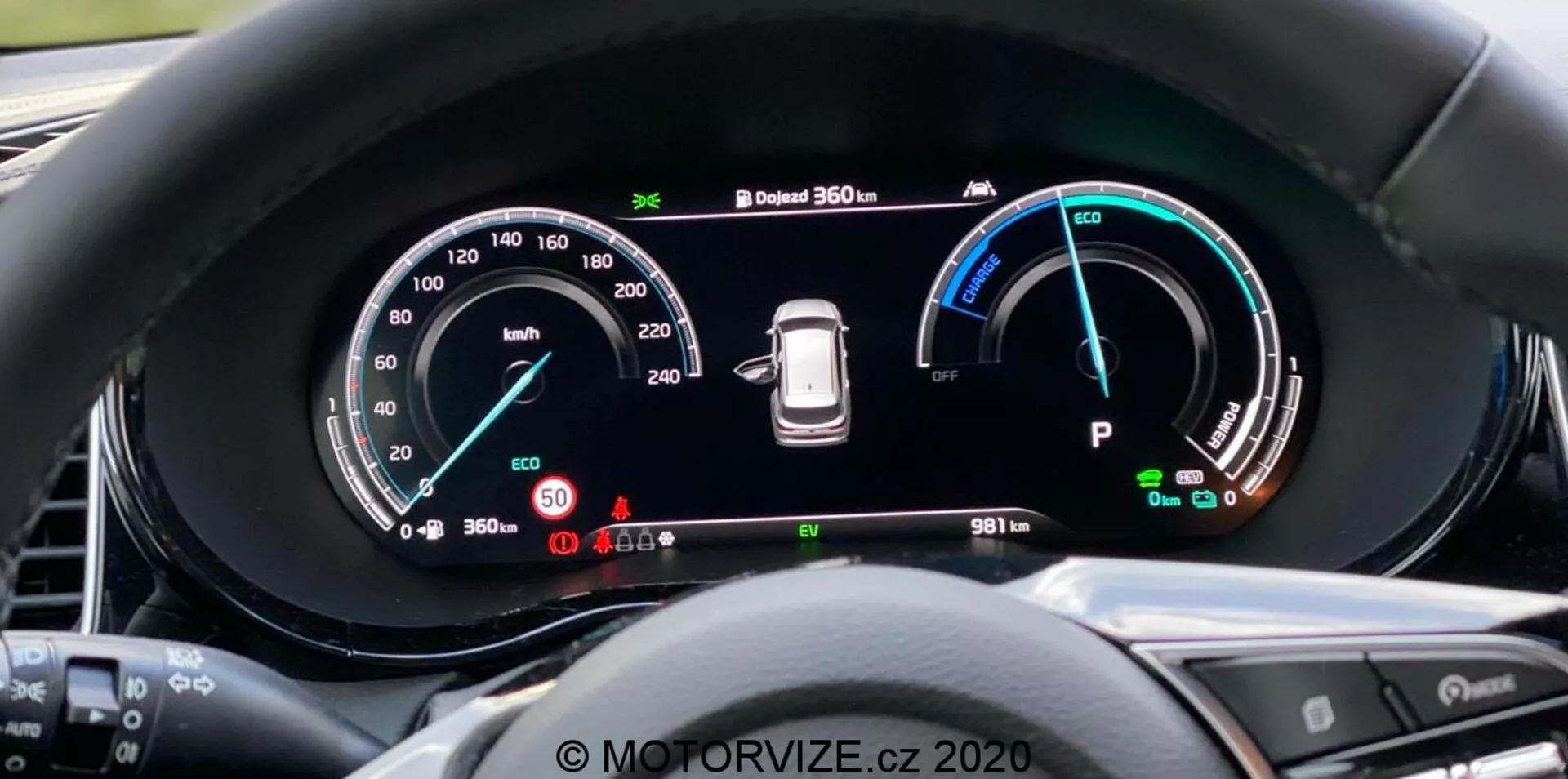 Close-up do painel de instrumentos digital do Kia Ceed 2018 a partir da perspectiva do motorista, com um grande display widescreen e instrumentação detalhada, incluindo um velocímetro até 260 km/h, indicador de potência com modos Eco, Comfort e Power, aviso de pressão dos pneus e indicador do modo 'Park'. O painel também exibe um sistema de câmera de 360 graus e um hodômetro mostrando 9811 km. A borda circundante reduz o reflexo e os botões do volante são parcialmente visíveis. Marca d'água 'MOTORVIZE.cz 2020'.