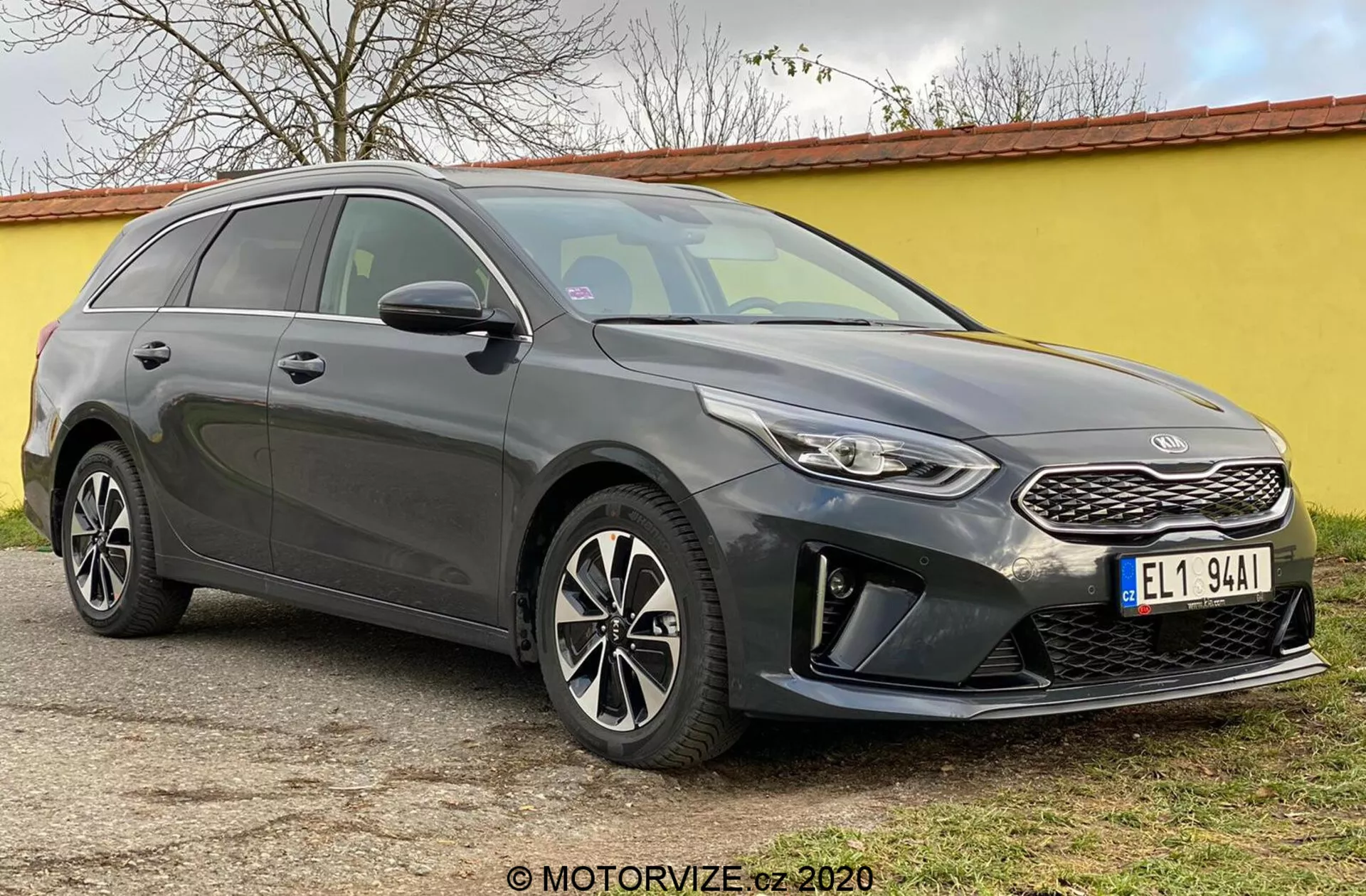 A imagem mostra o Kia Ceed 2018, uma perua moderna capturada de um ângulo frontal de três quartos, destacando sua fachada dianteira, incluindo uma grade estruturada com um emblema de marca distinto, faróis estreitos que se estendem para trás com luzes diurnas de LED e um para-choque dianteiro com alojamentos de luzes de neblina e sensores de estacionamento. As elegantes linhas de contorno do capô levam a um para-brisa inclinado, acentuando o perfil aerodinâmico do carro. Rodas de liga leve multi-raios e espelhos laterais com indicadores de direção integrados são visíveis, junto com uma linha de teto inclinada em direção à parte traseira e barras de teto, enfatizando tanto estilo quanto utilidade. Janelas escurecidas e linhas de carroceria ao longo da lateral adicionam uma aparência esculpida. O carro está parado em uma superfície plana ao ar livre.