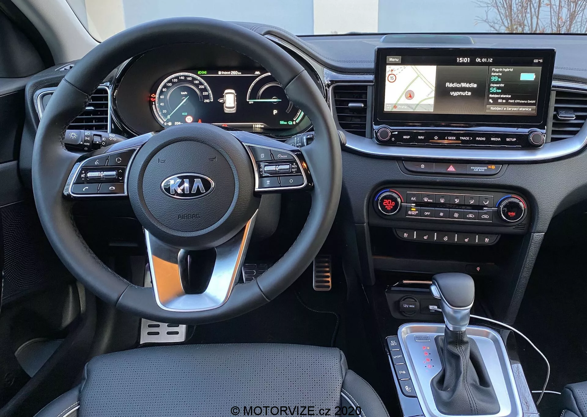 Vista interior de um Kia Ceed 2018 a partir da perspectiva do condutor, mostrando um volante de três raios com o logotipo da Kia, controles montados no volante, um painel de instrumentos digital/analógico, um display de infotainment flutuante com navegação e interface de mídia, controles físicos do sistema de climatização e uma alavanca de câmbio automático com possível seletor de modo de condução ou freio de estacionamento eletrônico.