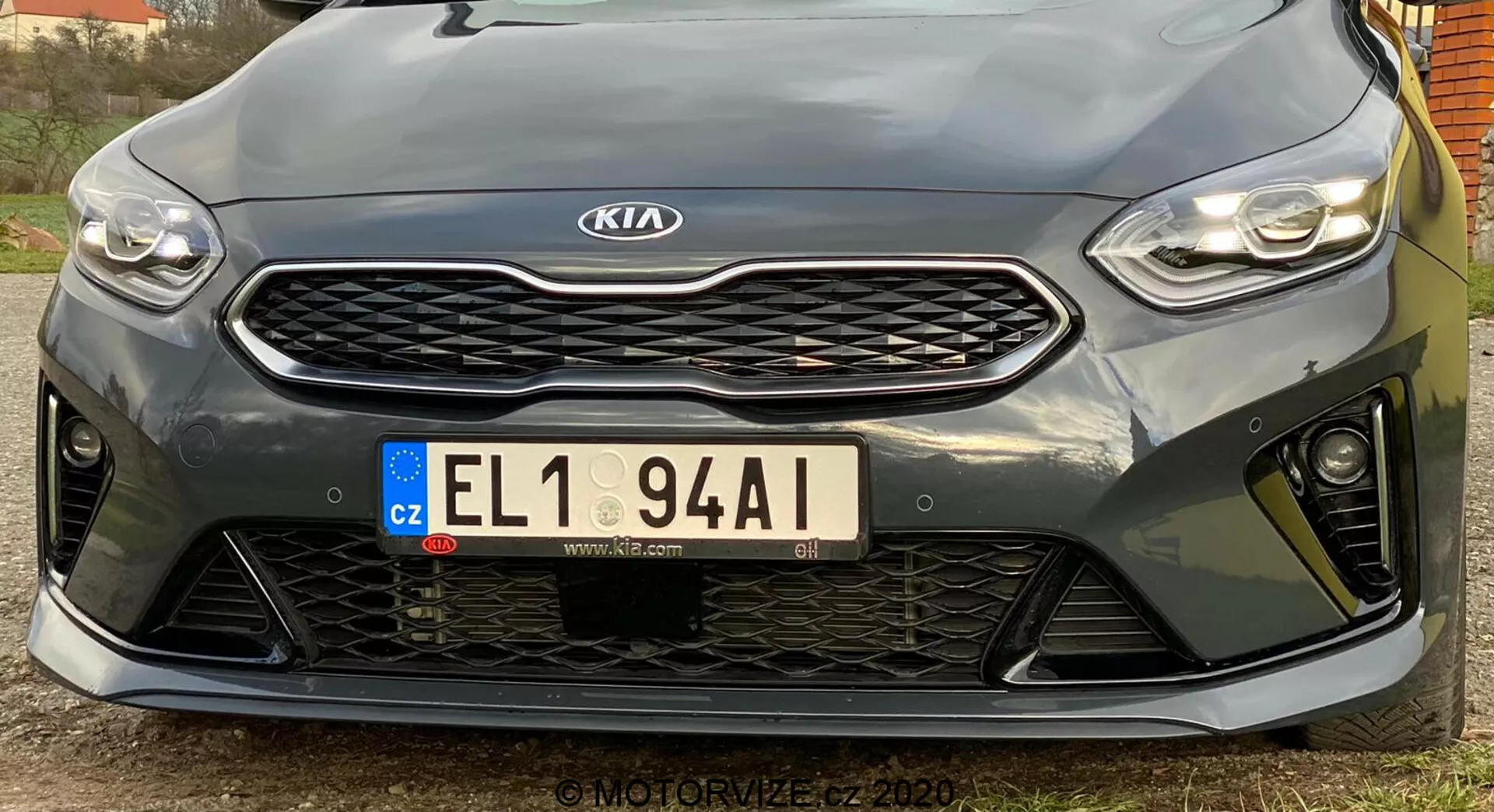 Esta imagem mostra a frente de um Kia Ceed 2018 tirada de um ângulo baixo. Destaca os faróis horizontais e elegantes com tecnologia LED, a grade proeminente com padrão colmeia e o emblema Kia centralizado, a placa de matrícula europeia da República Tcheca e o para-choque dianteiro esportivo com grandes aberturas. A vista aproximada destaca os sensores de estacionamento abaixo da grade. O design esportivo sugere um nível de acabamento de maior desempenho, embora as especificações exatas não sejam claras. A imagem de alta resolução captura detalhes e contornos do design, com um ângulo ligeiramente deslocado para a esquerda.