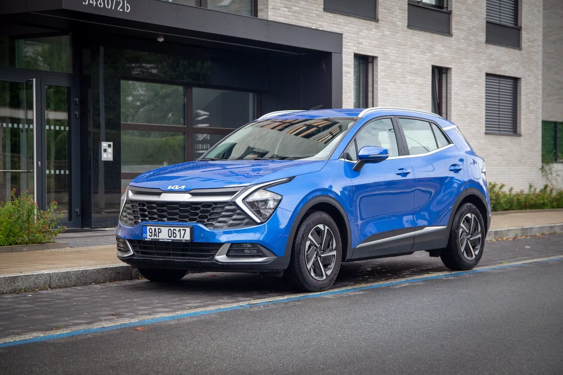 Kia Sportage 2022 em azul, com vista frontal de três quartos em uma rua urbana, destacando sua alta altura do solo, faróis LED, rodas de liga leve e tecnologia de segurança moderna.