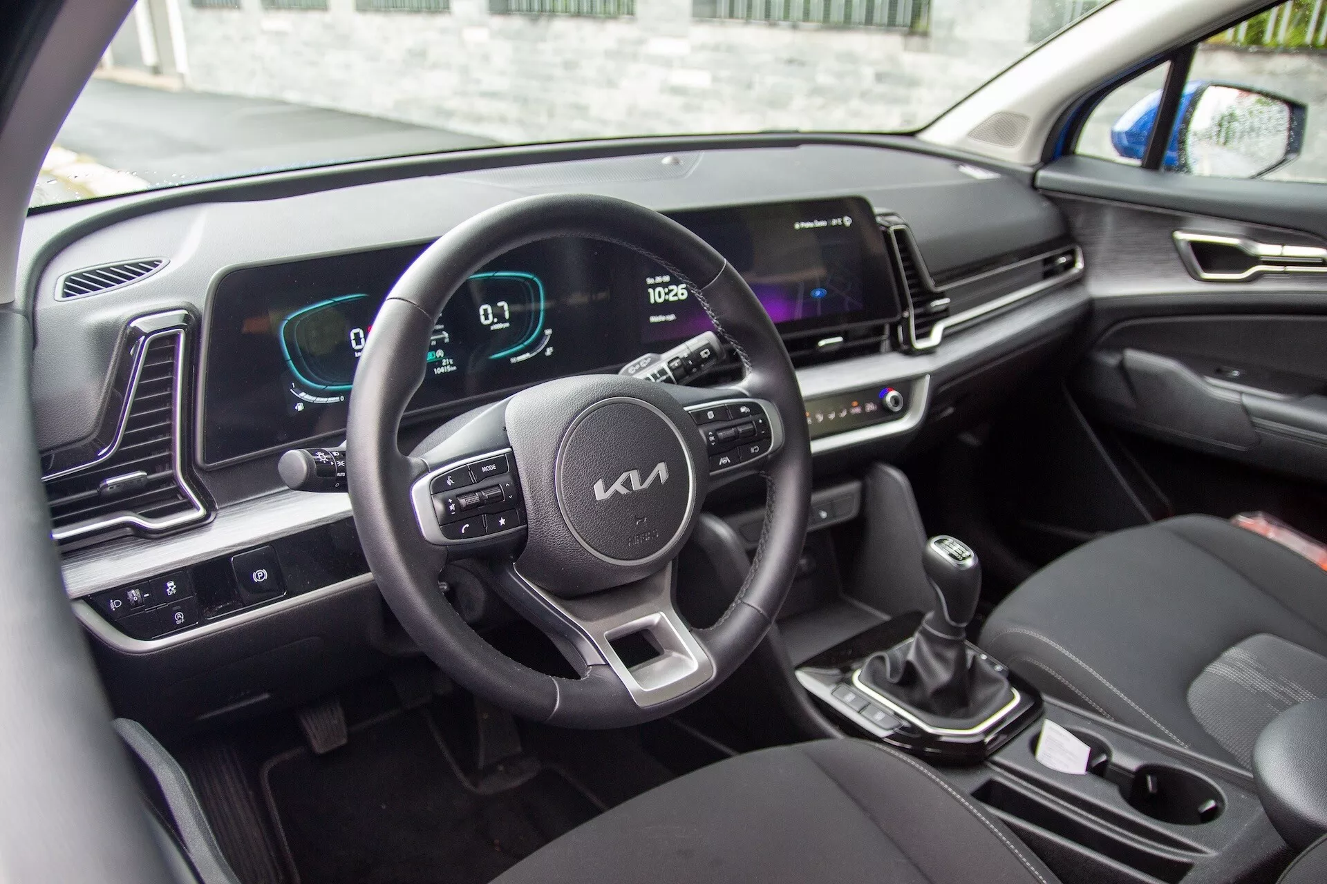 Interior do Kia Sportage 2022 mostrando volante com botões de controle, painel de instrumentos digital e tela de infotenimento