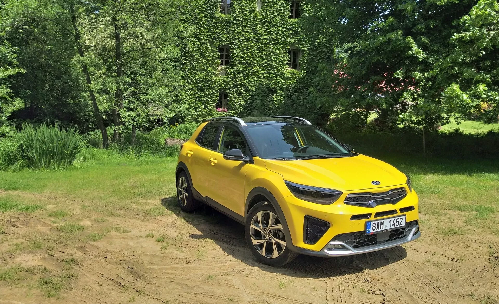 SUV crossover amarelo vibrante Kia Stonic 2017 em vista frontal de três quartos destacando sua grade frontal, faróis de LED, capô e lado do motorista, situado contra um fundo natural com luz solar em terreno limpo, mostrando capacidades fora de estrada, rodas de liga leve esportivas e elementos de design moderno.