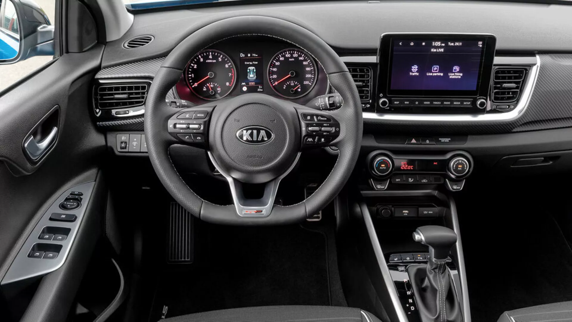 Vista interior de um Kia Stonic de 2017 a partir da perspectiva do passageiro, apresentando um volante de três raios com controles montados, cluster de instrumentos analógico-digital, sistema de infotenimento com tela sensível ao toque, controle de clima, transmissão automática e seletor de modo de condução.