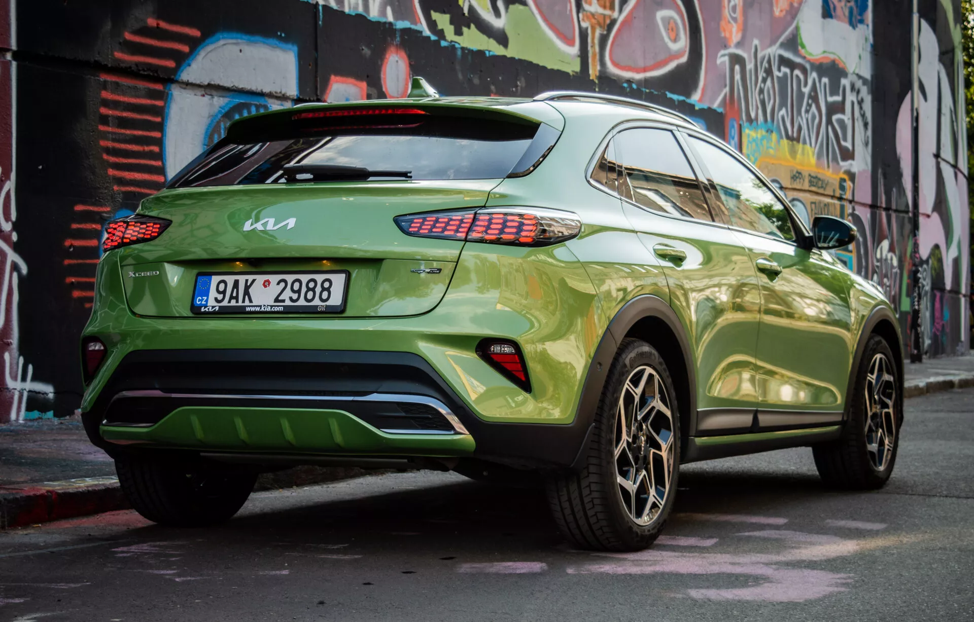 SUV crossover moderno Kia XCeed 2022 estacionado na diagonal mostrando seu quarto traseiro direito, com pintura verde vibrante e rodas de liga escura, demonstrando o perfil lateral do veículo, design traseiro, luzes traseiras LED, janelas com insulfilm, um spoiler no teto e um potencial difusor traseiro