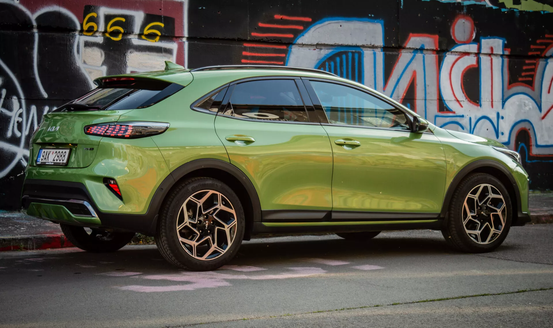 Vista lateral do Kia XCeed 2022 destacando o design da roda traseira, pintura verde metálica, luzes traseiras LED e estilo SUV compacto com características aerodinâmicas contra um pano de fundo de arte de rua urbana.