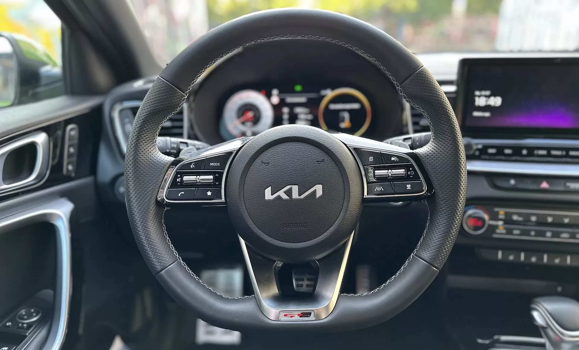 Vista da perspectiva do motorista dentro de um Kia Xceed 2022 mostrando o painel de instrumentos, volante com botões de controle, conjunto de instrumentos digital-analógico e console central multimídia