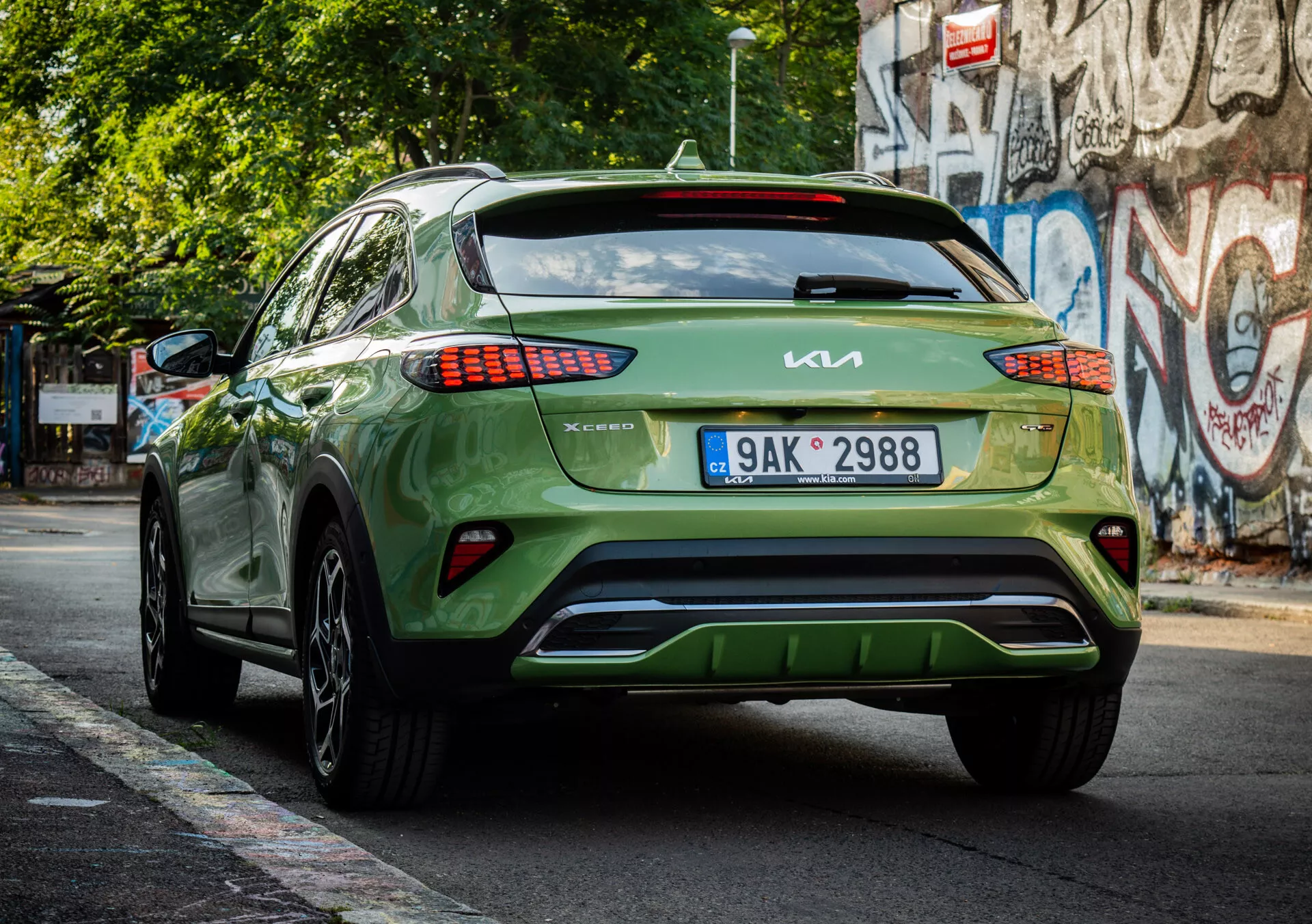 Vista traseira de um crossover/SUV Kia XCeed verde de 2022 mostrando marca, design de luz traseira LED, colocação de placa de licença, estética do para-choque inferior e acabamento brilhante em uma rua urbana.