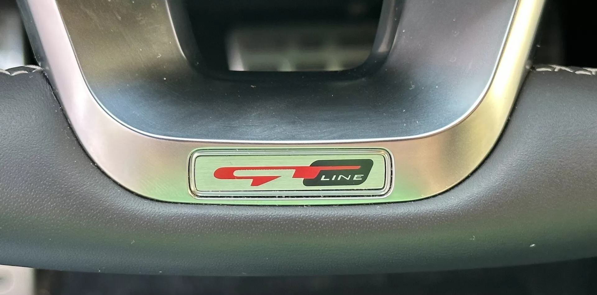 Close-up do emblema do volante Kia XCeed 2022 GT-Line exibindo letras metálicas e pretas com um toque vermelho esportivo, cercado por um volante premium de couro e metal