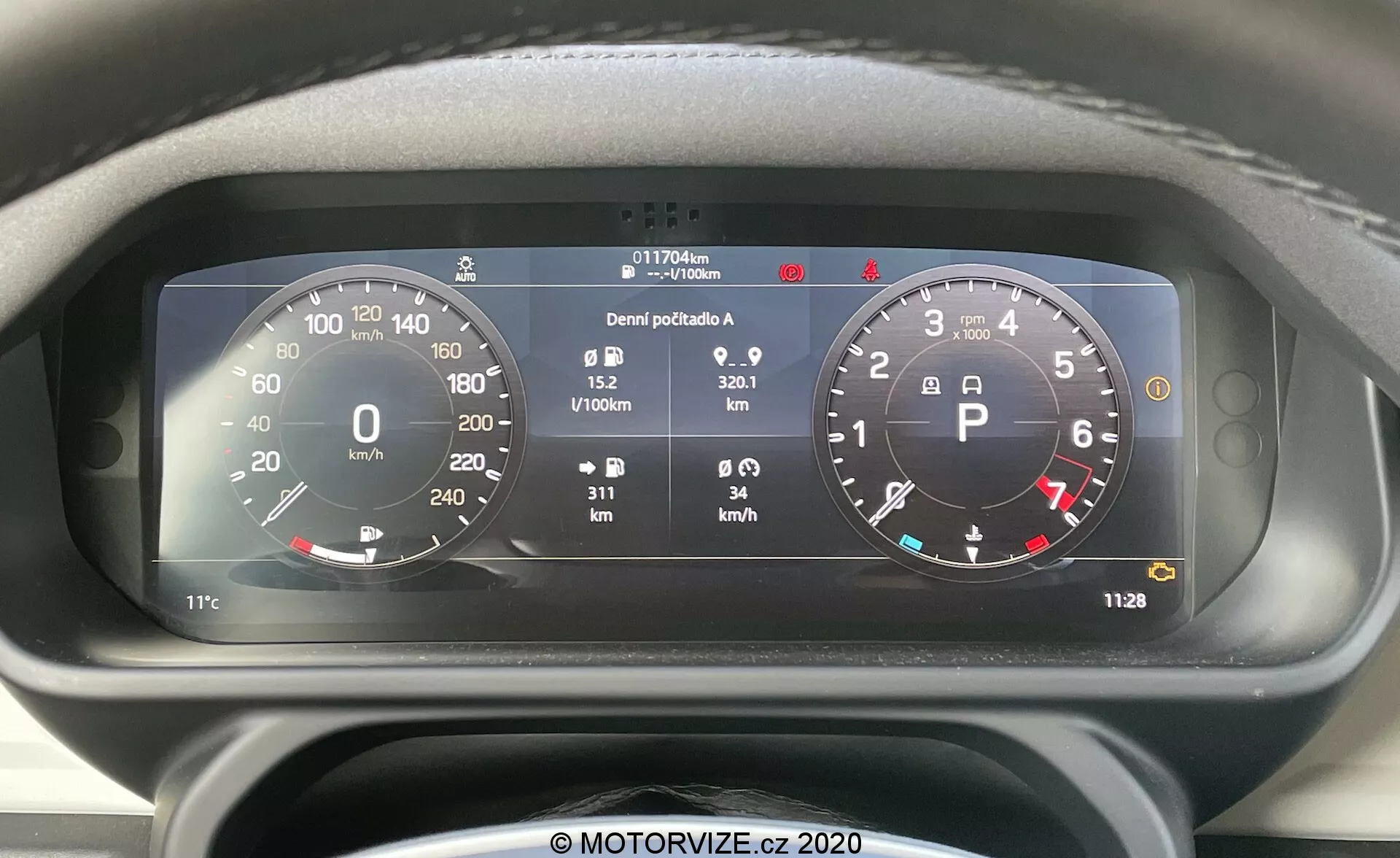 Imagem de close, vista frontal do painel de instrumentos digital do Land Rover Defender 2020 com velocímetro circular proeminente (0-260 km/h) e conta-rotações (0-8,000 RPM), integração de vários indicadores de estado do veículo e informações detalhadas, incluindo medidor de combustível, temperatura, hodômetro (117,706 km), contagem de viagens, consumo médio de combustível (0.9 L/100km), velocidade média (32.1 km/h) e relógio digital (11:28).