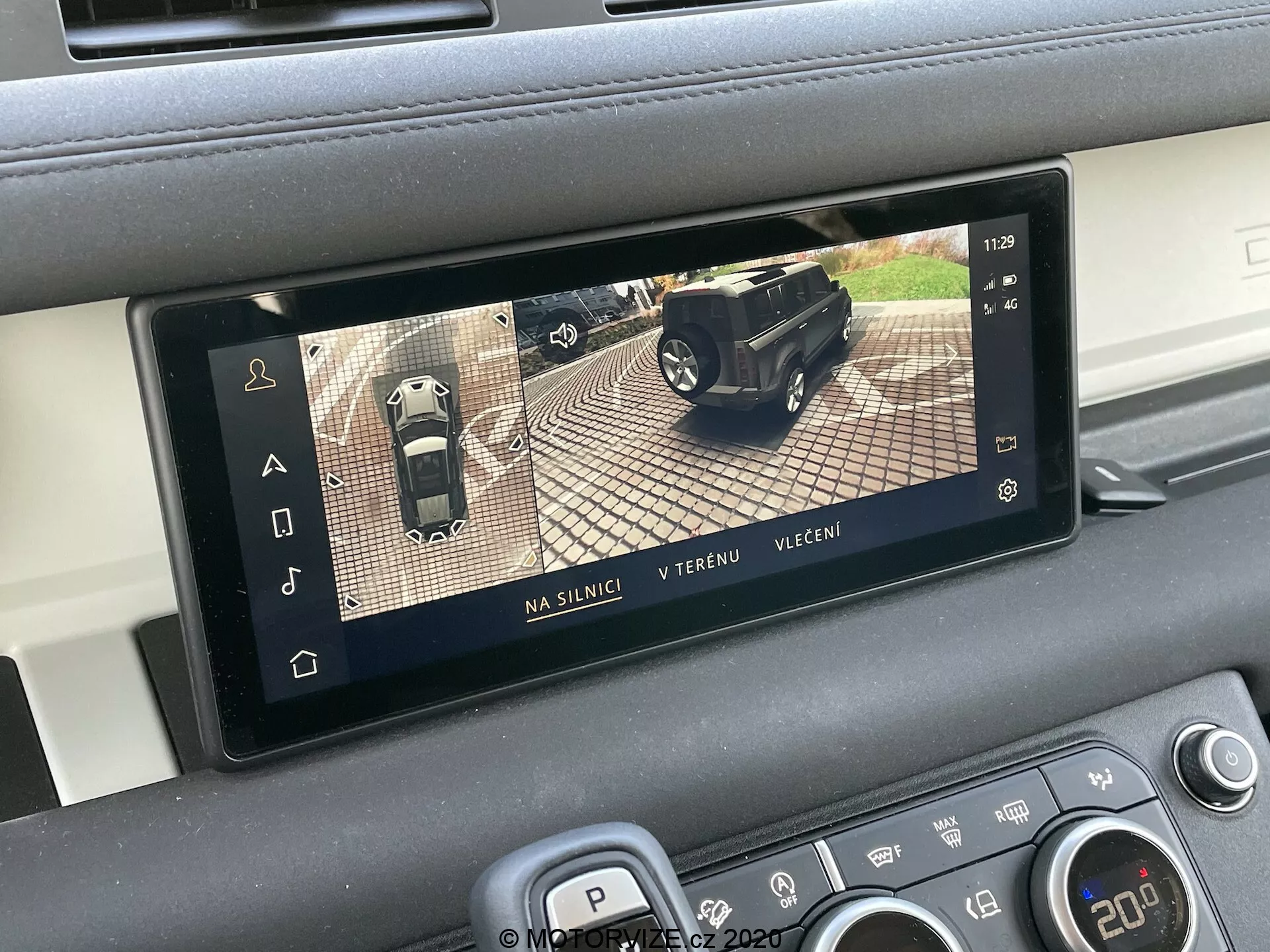 Display interno do Land Rover Defender 2020 apresentando um sistema de câmera de visão de 360 graus, parte dos sistemas avançados de assistência ao motorista (ADAS). A tela retangular está integrada no console central do veículo e mostra três modos de exibição: rodoviário, off-road e noturno. A tela ajuda no estacionamento e manobras, combinando imagens de várias câmeras ao redor do carro.
