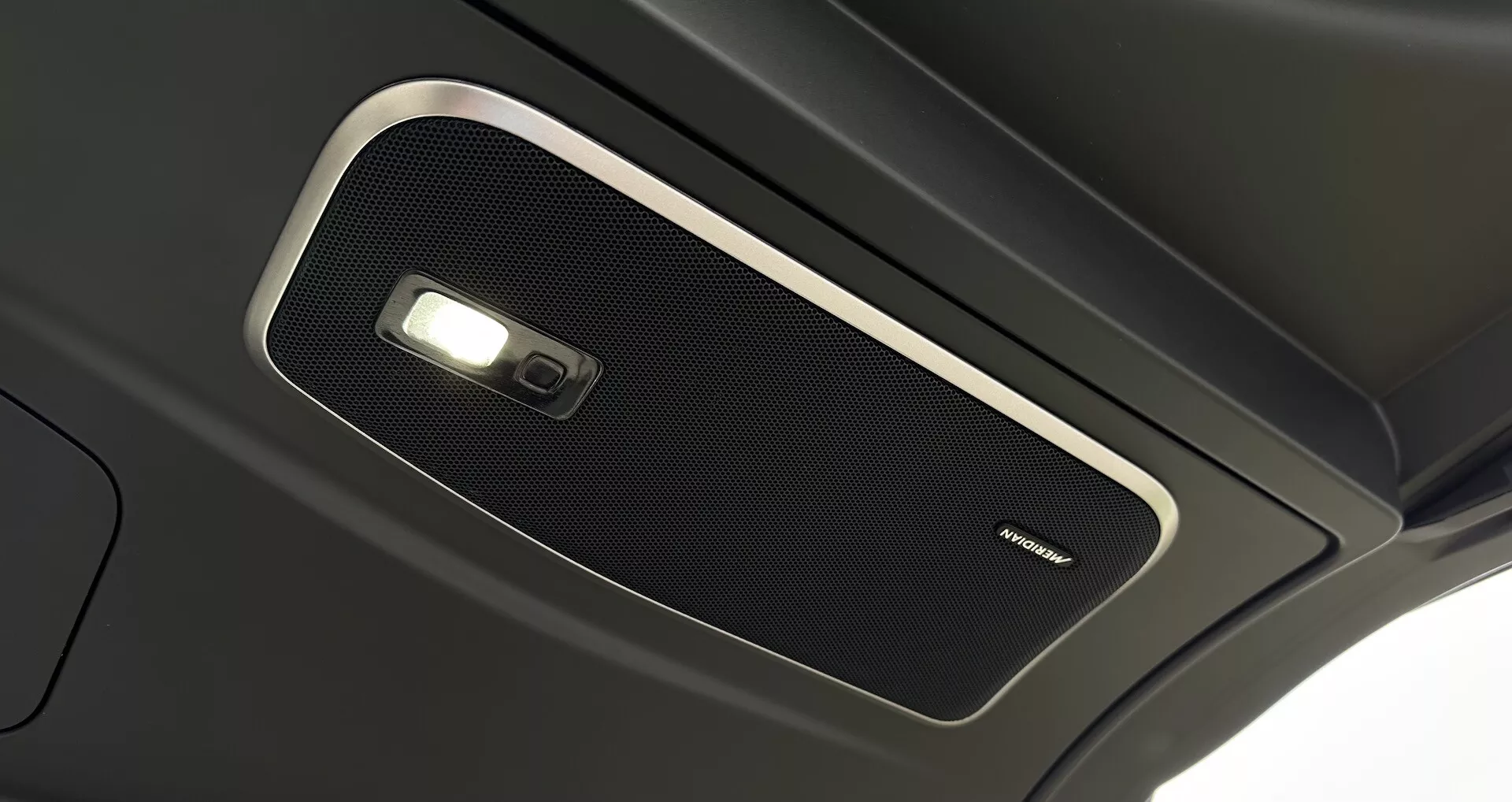 Vista de perto do console superior interno do Range Rover 2021, mostrando uma grade de alto-falante de alta qualidade e luz de domo, enfatizando a acústica premium da cabine e a tecnologia avançada de iluminação interna.