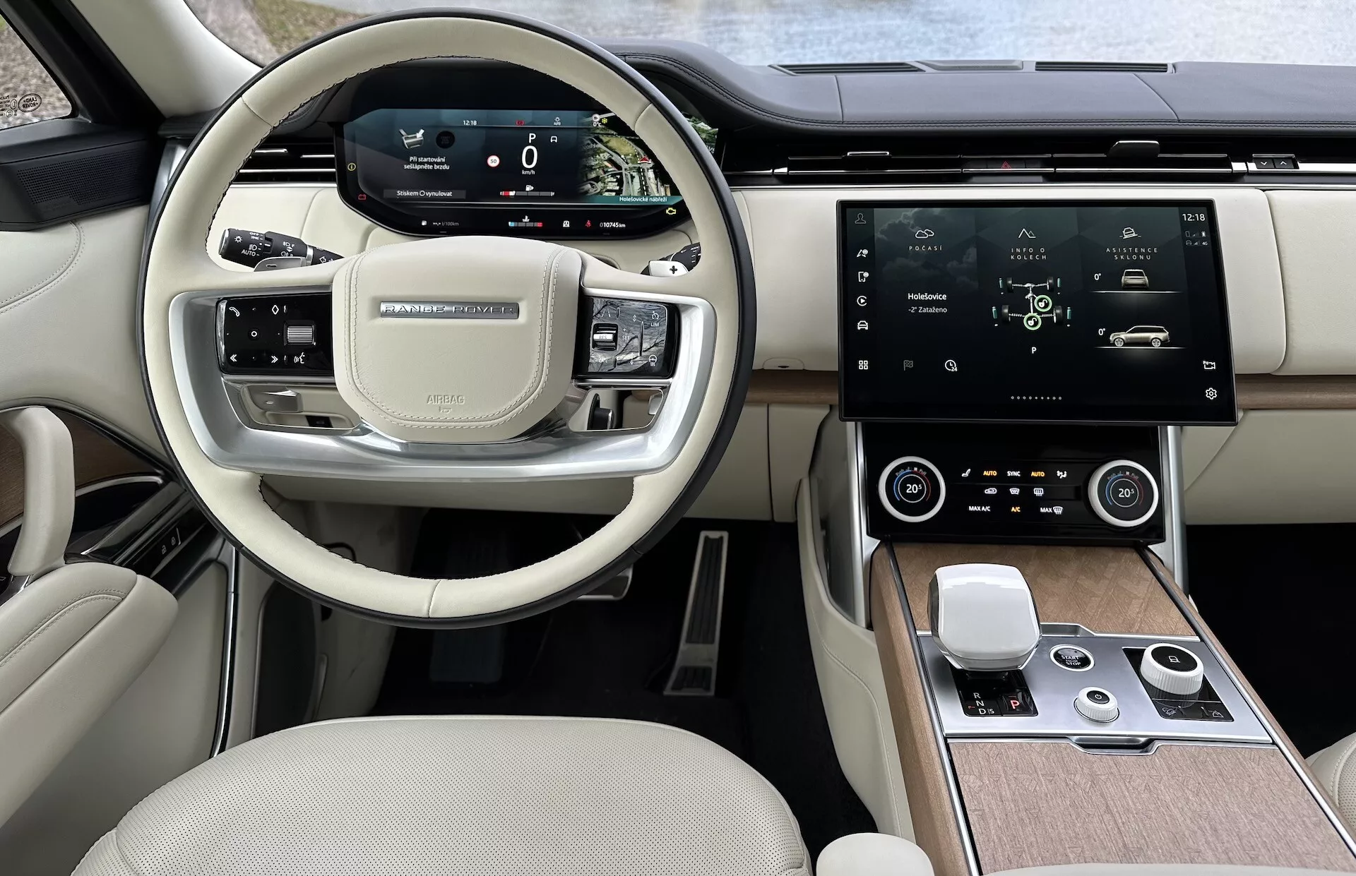 Vista interior do Land Rover Range Rover 2021 mostrando o volante moderno com botões multifuncionais, cluster de instrumentos digital, grande tela touchscreen central para infotainment, controle automático do clima e design de cabine de dois tons de luxo