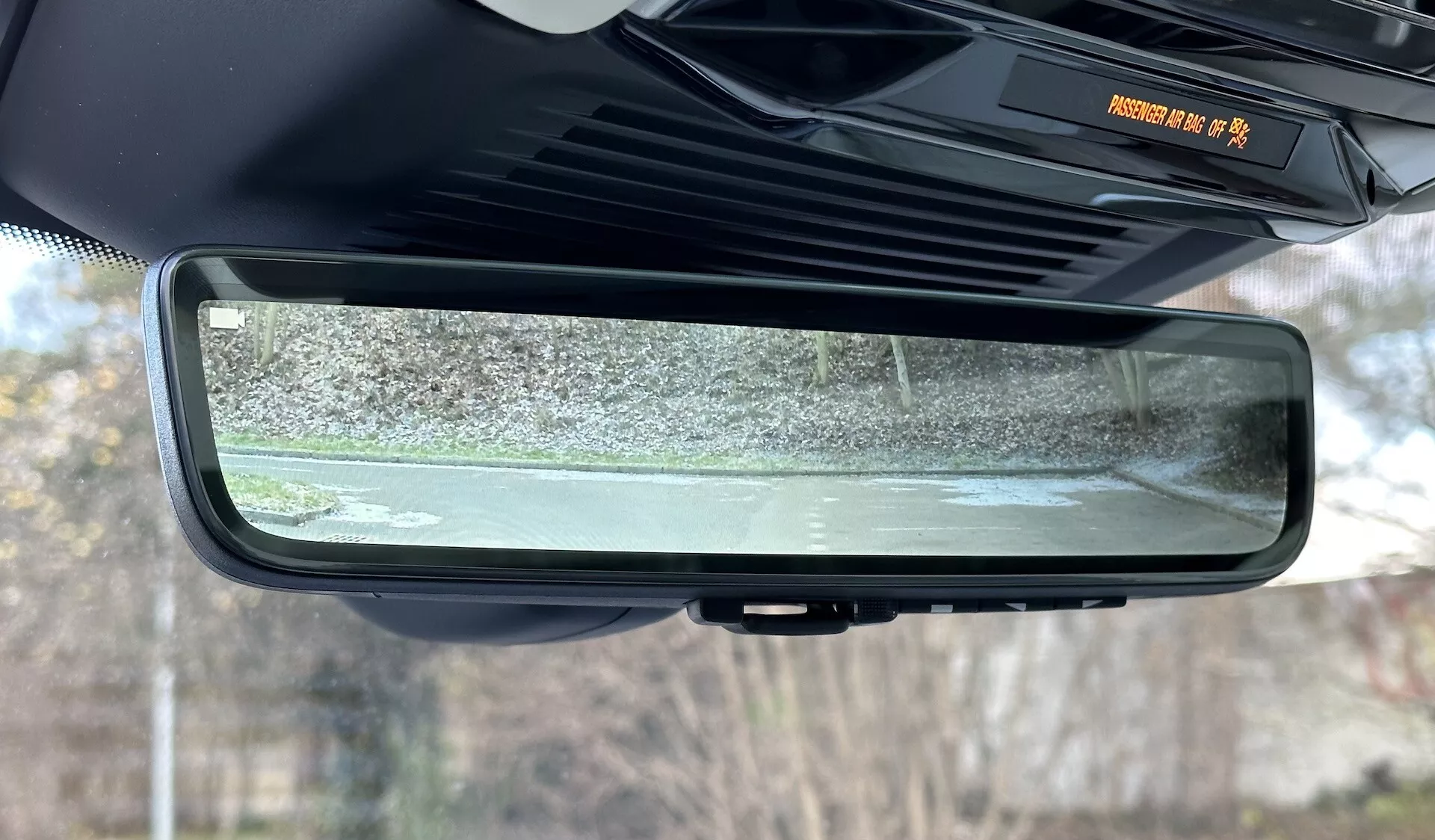Vista detalhada do espelho retrovisor auto-dimável eletrocromático dentro de um Range Rover 2021, destacando seu design sem moldura, características da cabine interior e a cena refletida dos arredores externos estacionários