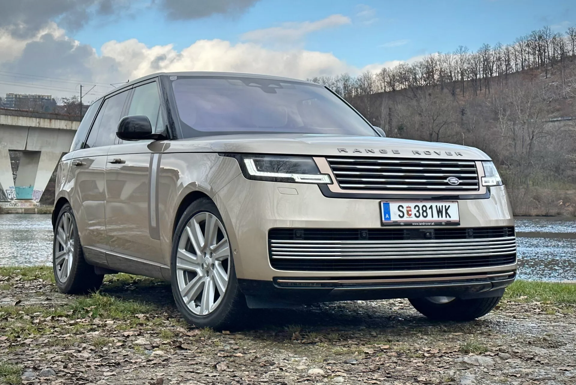 SUV de luxo Land Rover Range Rover 2021, vista frontal de três quartos destacando a grade cromada, faróis LED, rodas de liga leve multirradiadas e design aerodinâmico, estacionado ao ar livre perto de um rio e uma ponte
