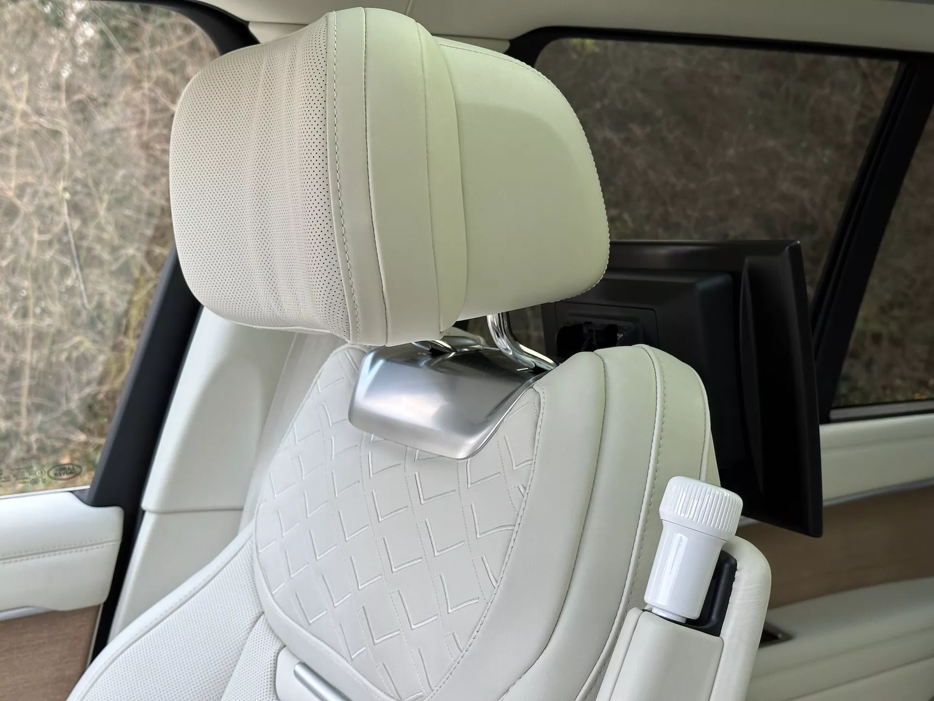 Vista interior do Land Rover Range Rover 2021 destacando o assento do passageiro em couro creme acolchoado com suporte para cabeça em cromo e porta-garrafas na porta, exibindo design de veículo de luxo e recursos de conforto