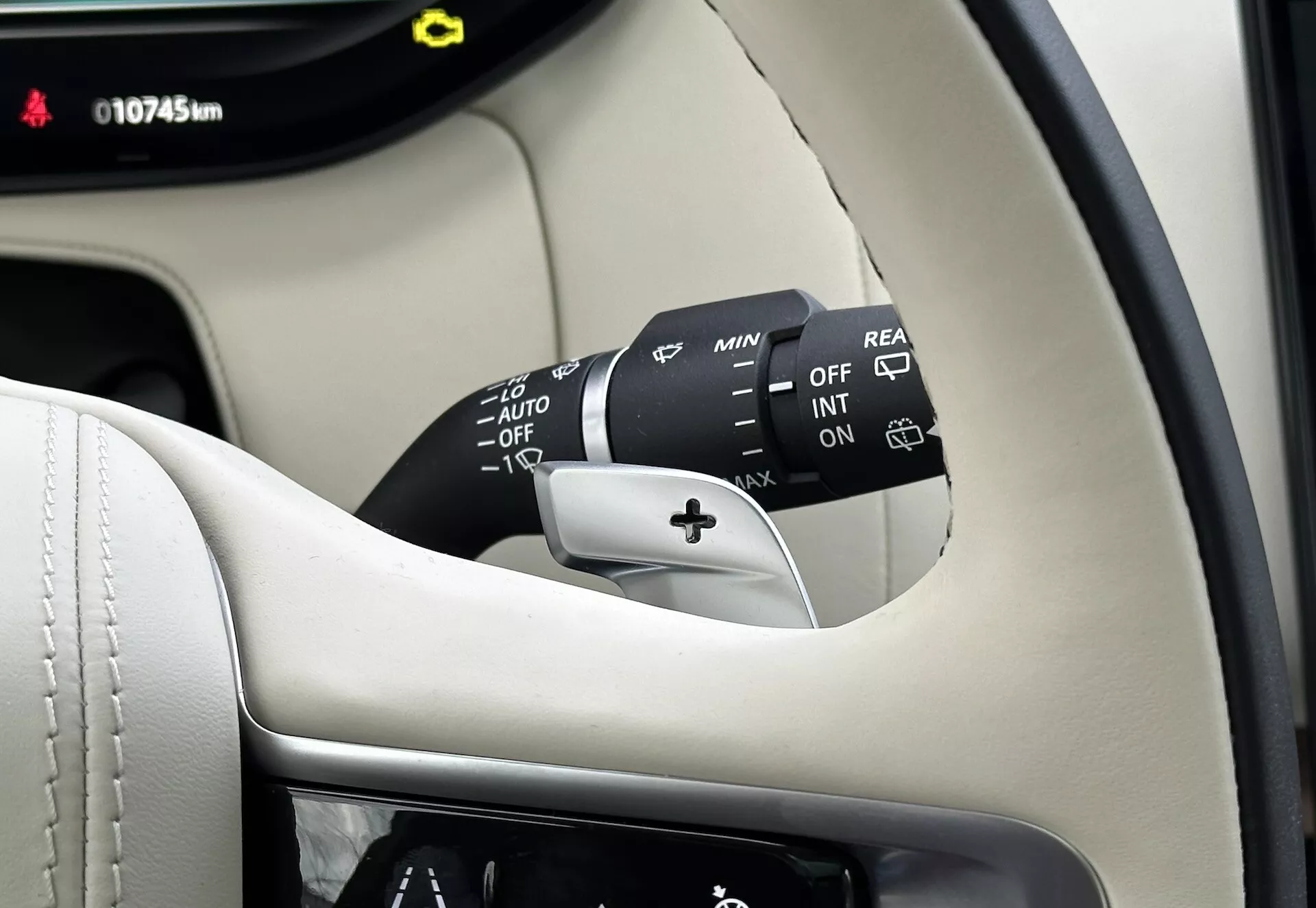 Vista detalhada do interior da Land-Rover Range-Rover 2021 mostrando a coluna do volante, a haste de controle do limpador de para-brisa com múltiplas configurações incluindo DESL, INT, LIG, ajustadores de velocidade e AUTO para limpadores automáticos sensíveis à chuva, além de uma opção de limpador traseiro. Parte visível do painel de instrumentos exibe 10745 km, ambientado contra um interior premium preto e creme.