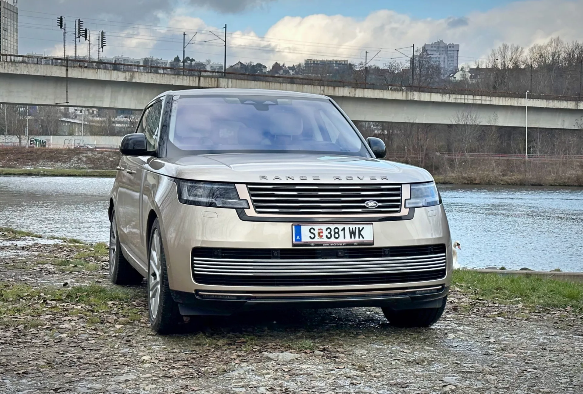 SUV de luxo Range Rover 2021 estacionado ao ar livre perto de um rio e ponte em um ambiente urbano, exibindo seu design moderno, grade frontal e faróis LED elegantes