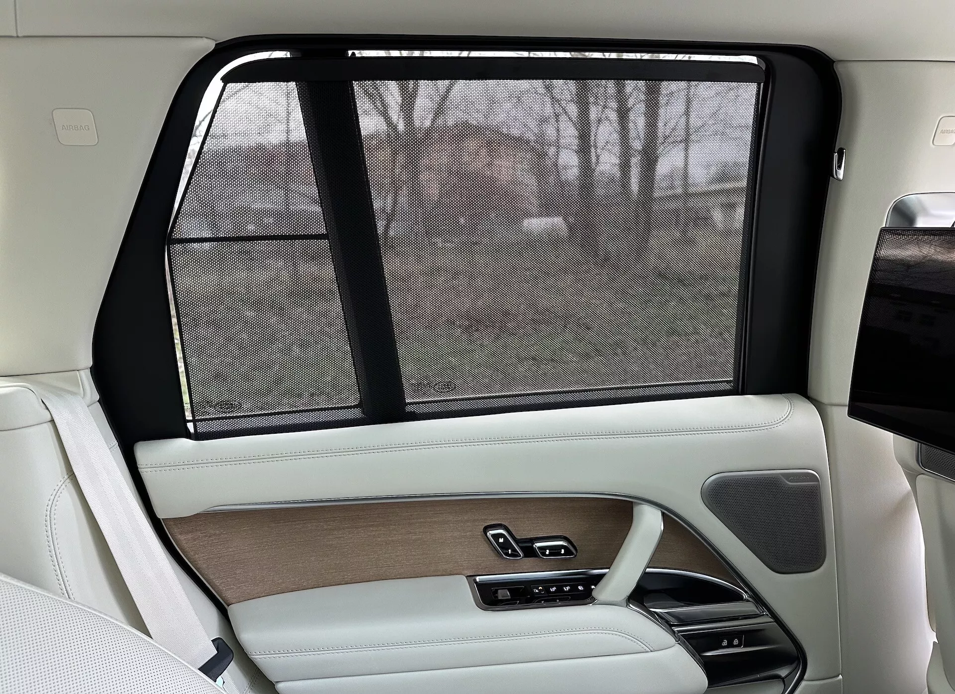 Interior do lado do passageiro traseiro de um Land Rover Range Rover 2021, apresentando um design luxuoso em bege e preto, acabamentos em madeira, acabamentos em couro, sombreado eletrônico e sistemas de controle avançados