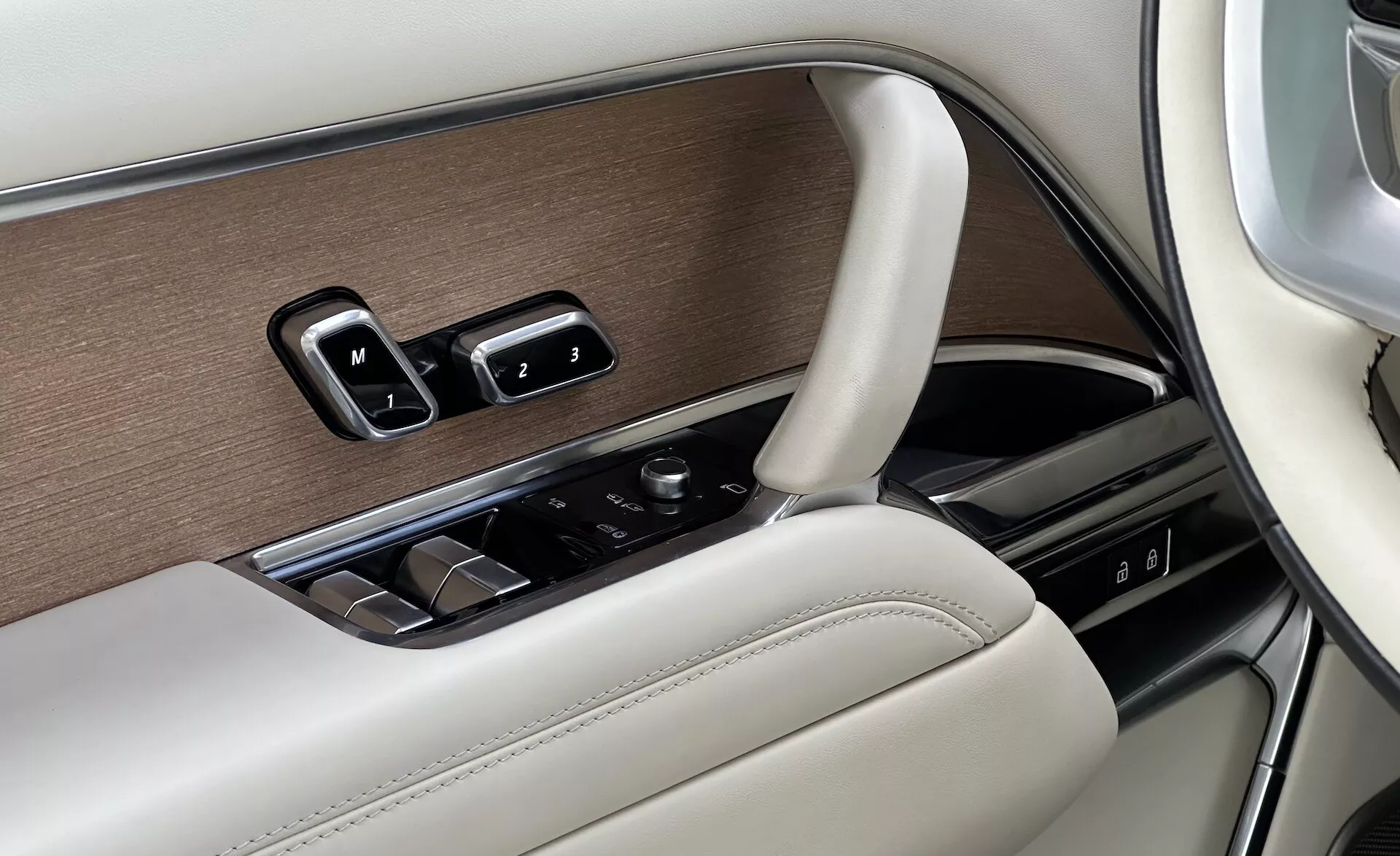 Detalhe do interior do Land Rover Range Rover 2021 mostrando o painel da porta do lado do motorista com controles de janela, ajustes de espelho, configurações de memória de assento em um design luxuoso com acabamentos em madeira, cromo e couro, e um botão de controle para o sistema de infotenimento.