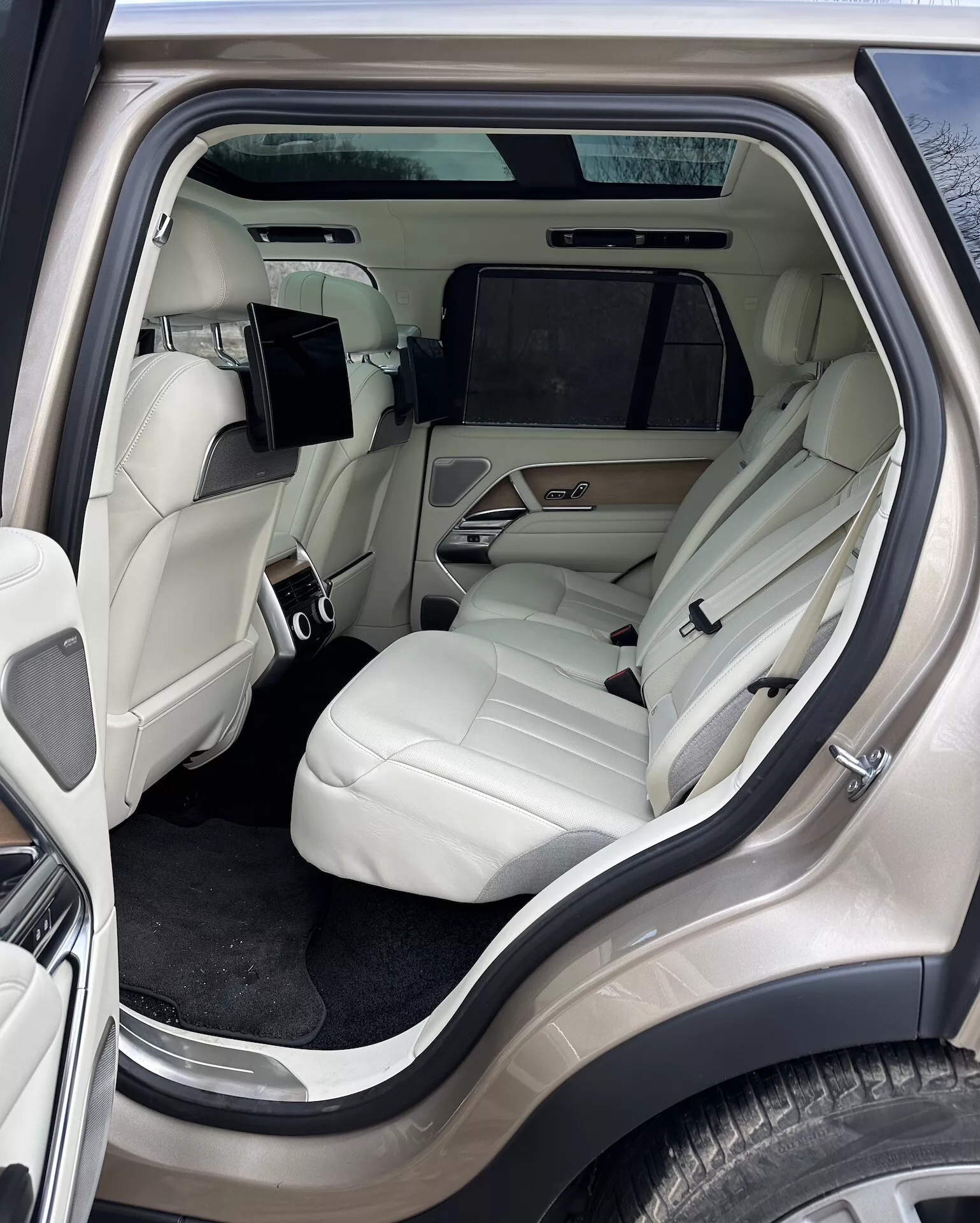 Vista interior do Land Rover Range Rover 2021 focada no luxuoso compartimento de passageiros traseiros de um ângulo lateral externo, apresentando assentos de couro de cor clara, console central avançado, sistema de entretenimento e detalhes de luxo